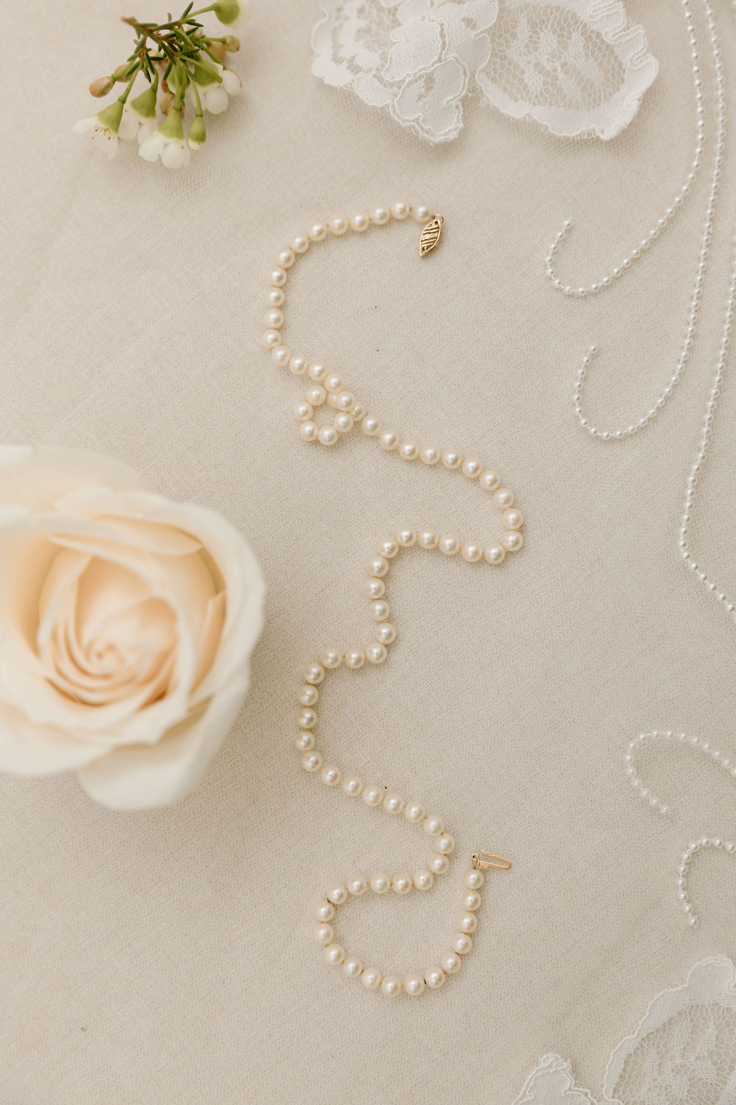 Delicate arrangement of peach roses and pearl necklaces on soft beige lace fabric creating an elegant wedding backdrop.