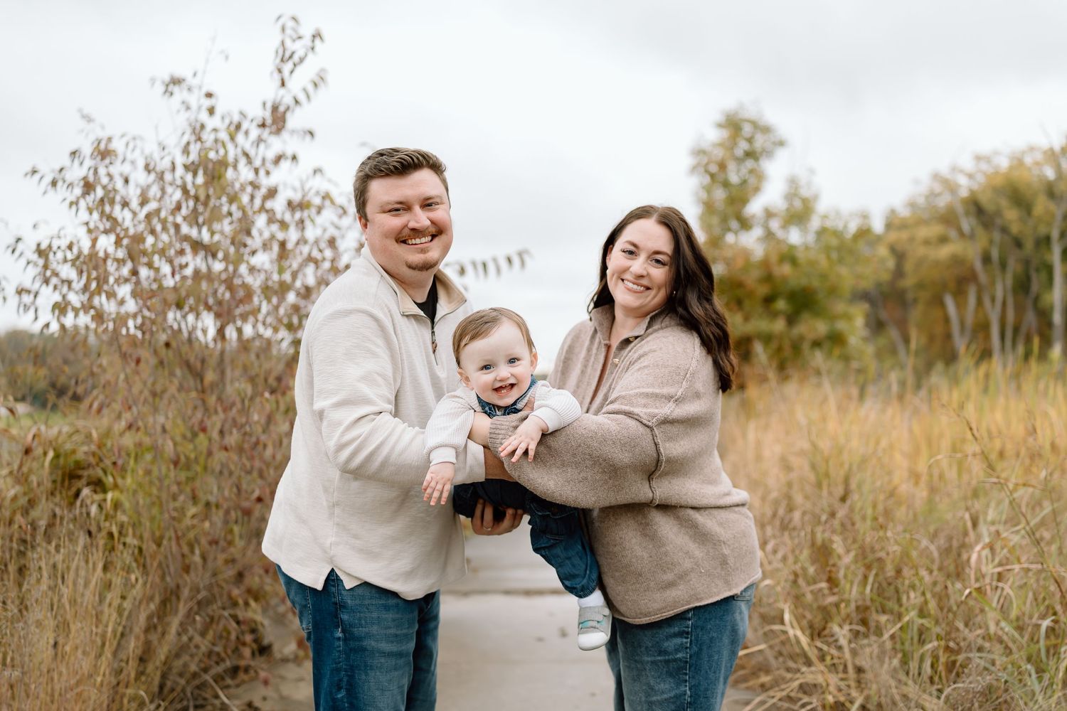 A family wearing coordinated beige and blue outfits embraces while laughing together in a fall field setting.