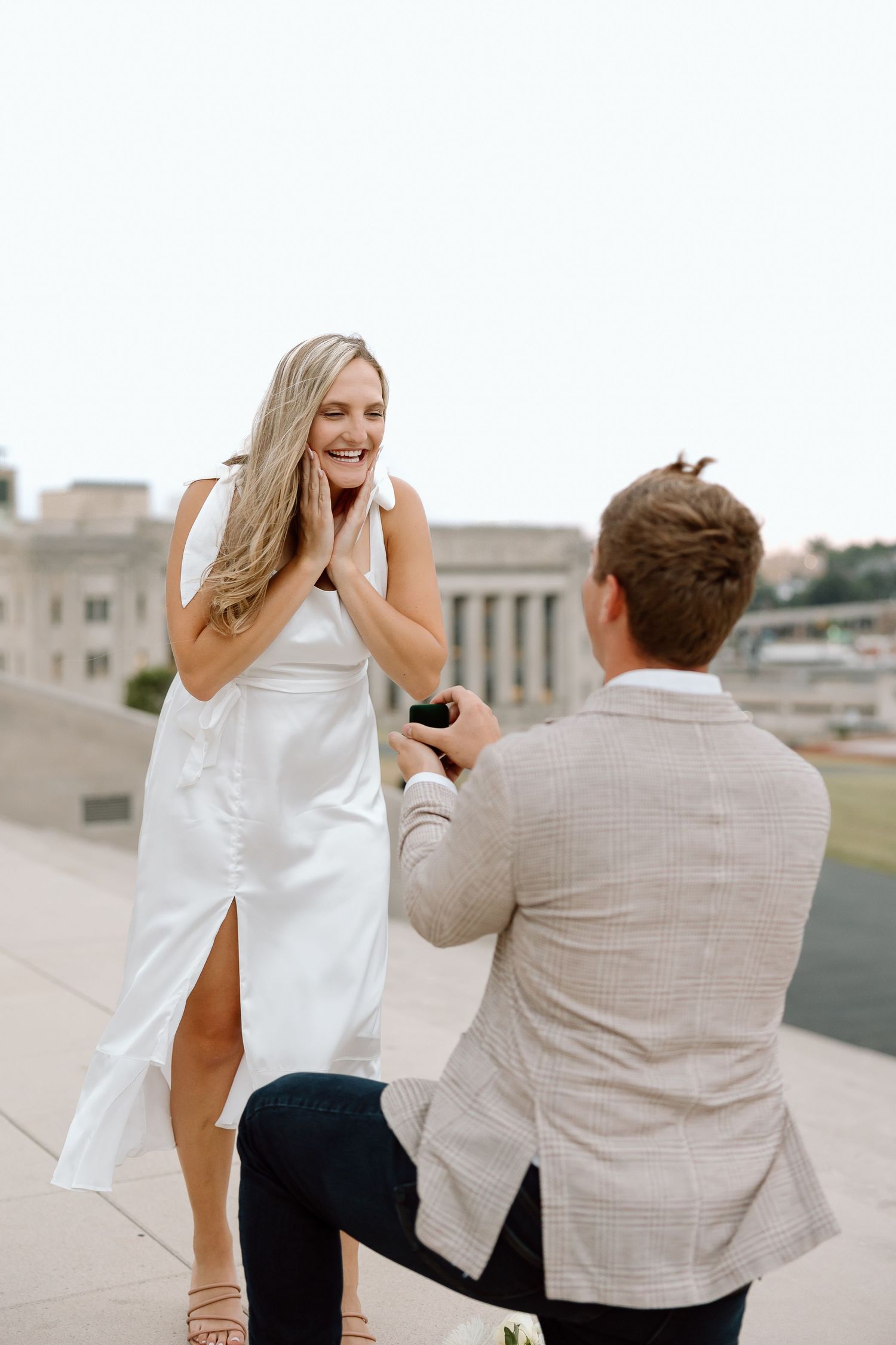 A couple shares a joyful moment during a rooftop proposal as she reacts with excitement and surprise.