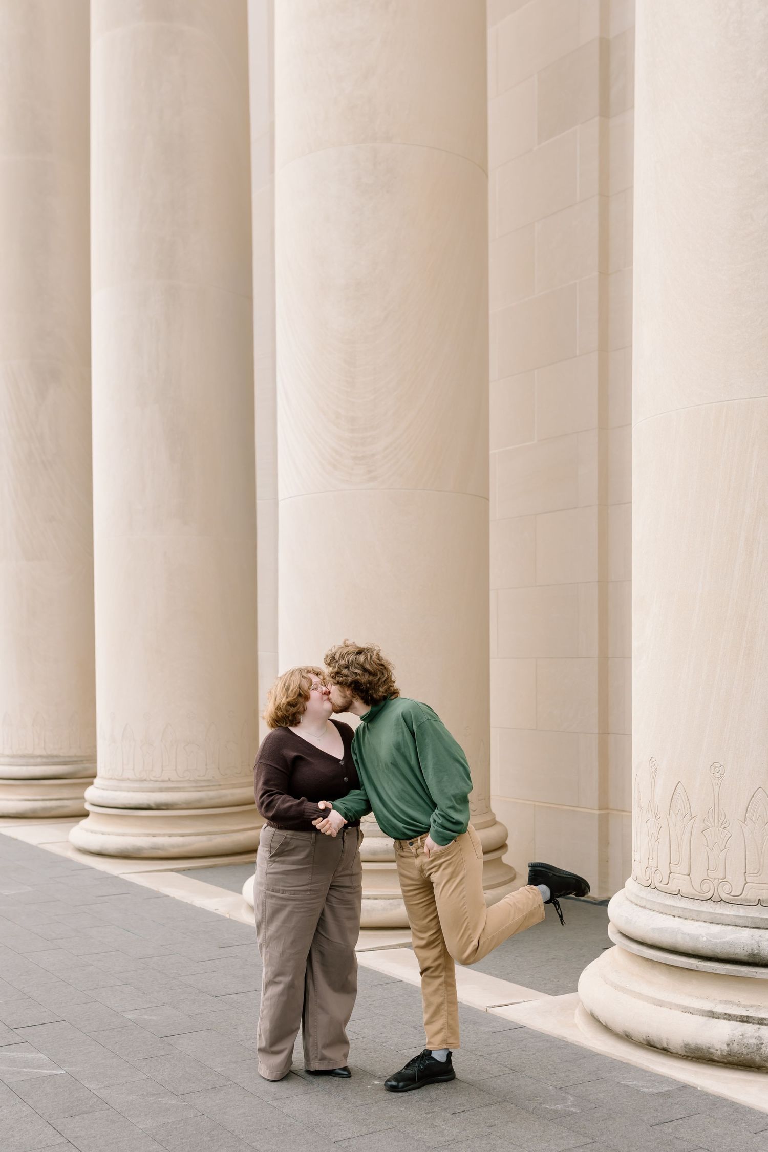 Romantic couple embracing between classic white columns in an architectural setting.