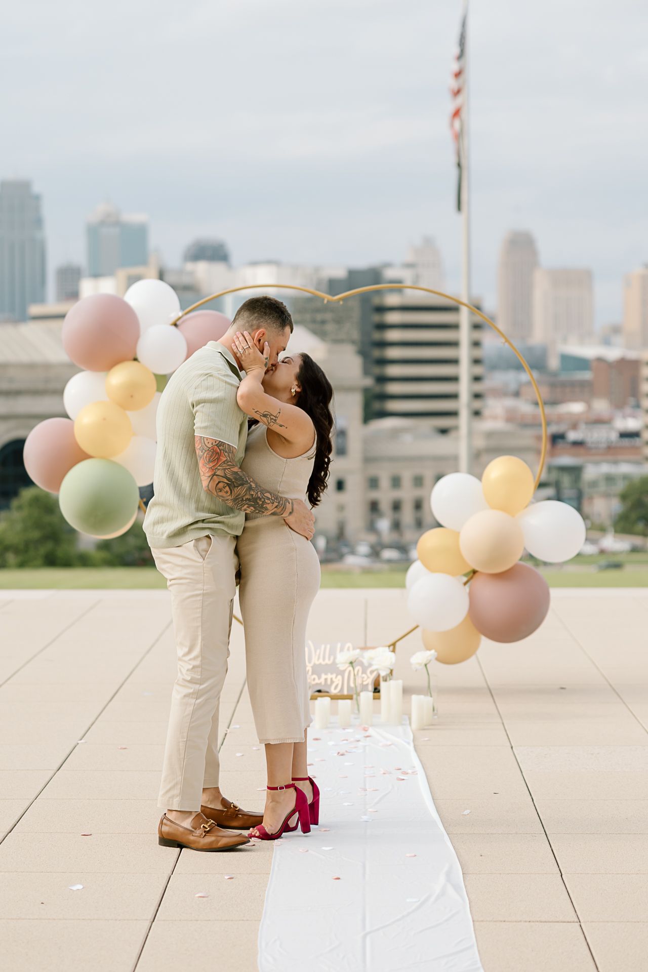 Two people embrace on an urban rooftop decorated with pastel balloons and white details.