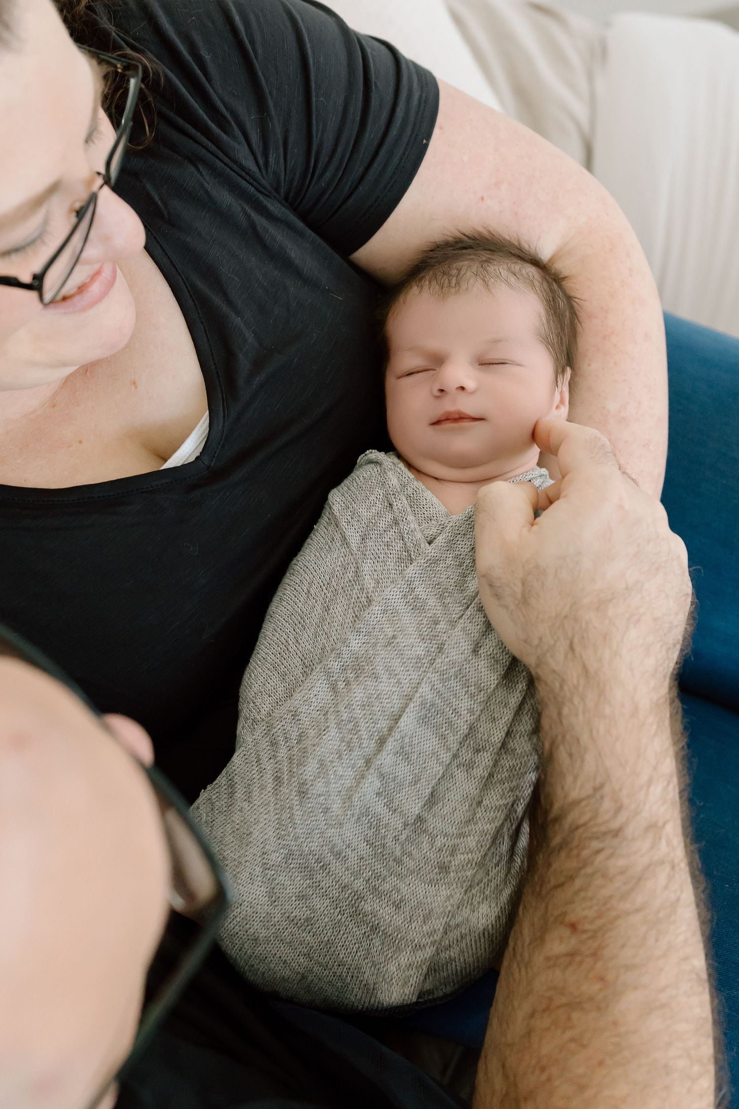 A sleeping baby wrapped in a gray knit blanket rests peacefully in a parent's arms.
