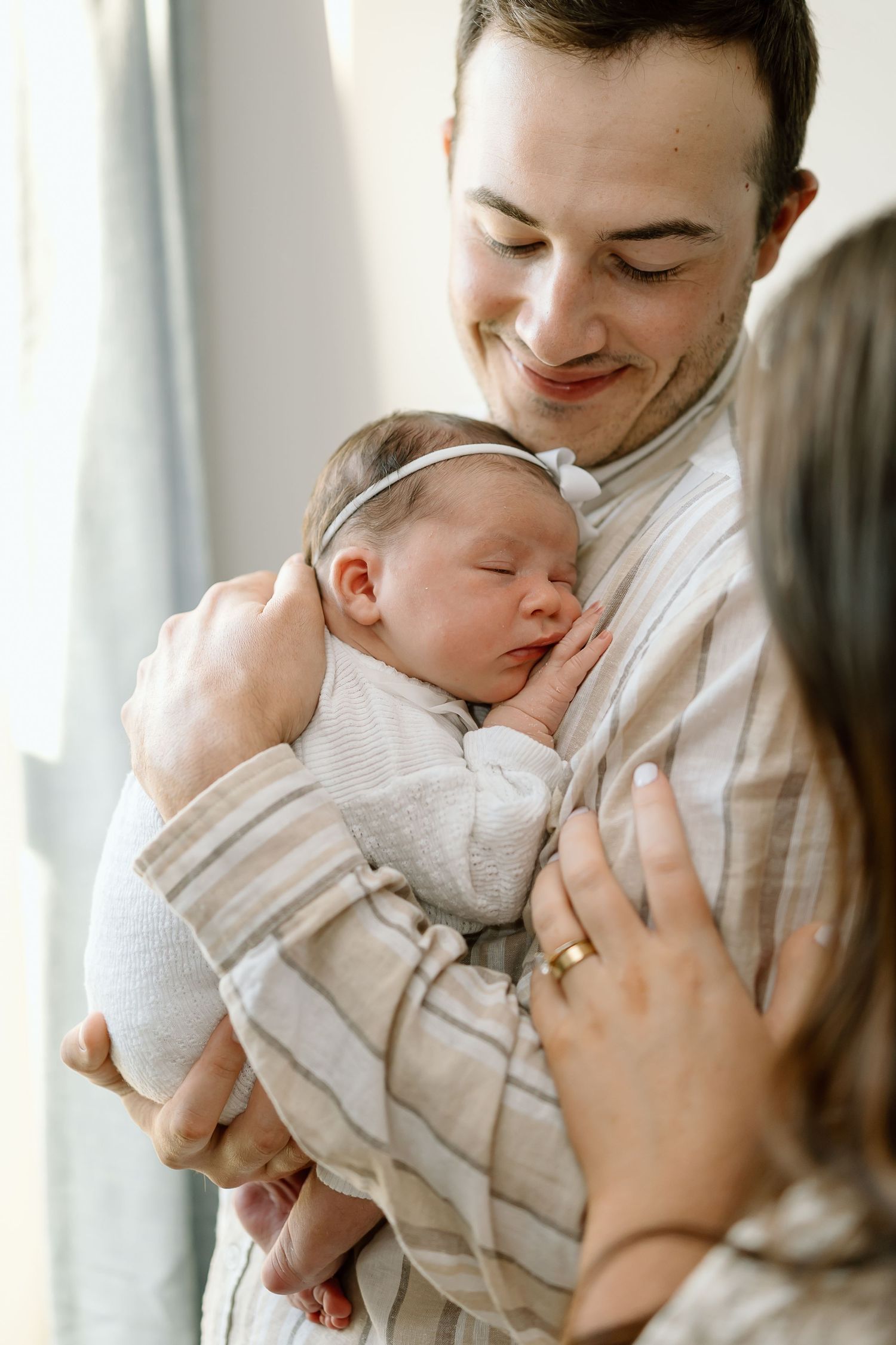 A tender moment as parents hold and gaze lovingly at their sleeping newborn baby in soft natural light.