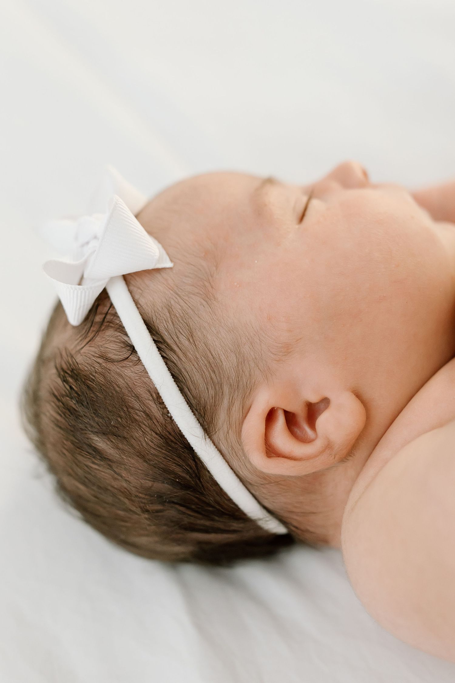 A baby wearing a white bow headband lies peacefully on a white background in a series of close-up shots.