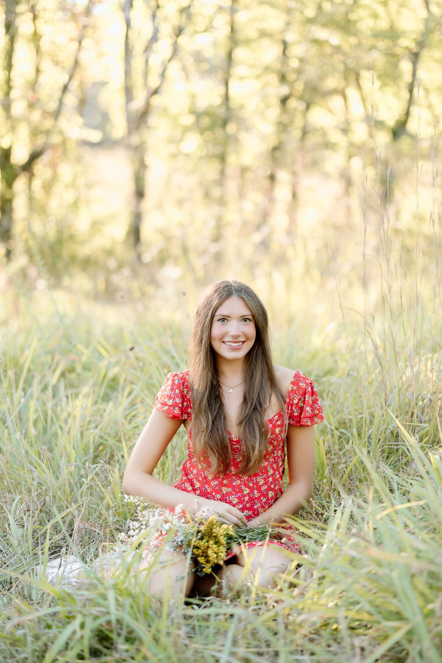 A person in a red polka dot dress sits in tall grass during golden hour with soft natural lighting.