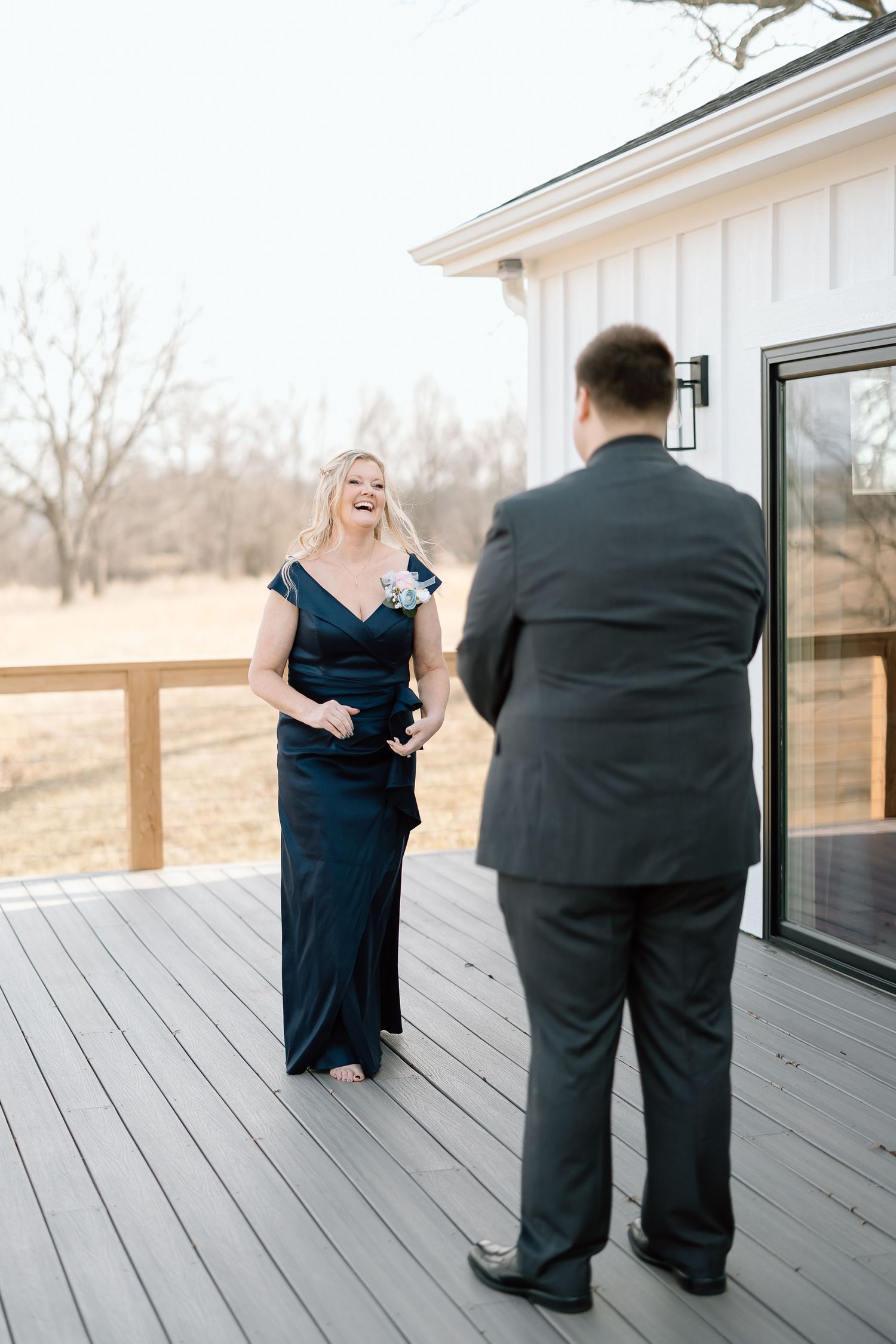 A couple in formal attire shares a sweet moment on a wooden deck overlooking a scenic winter landscape.