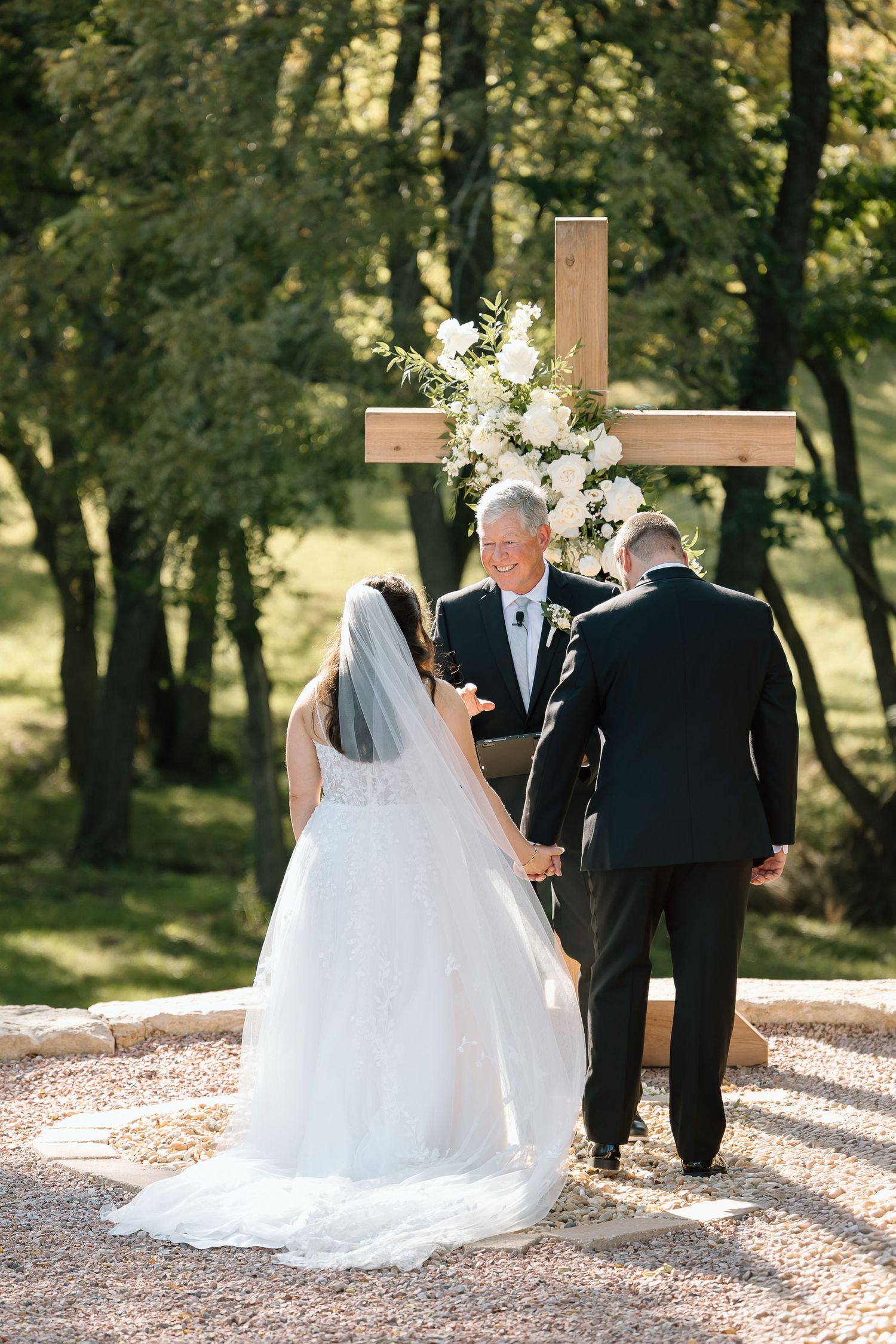 A wedding party walks along a sunlit path through a wooded area during an outdoor ceremony.