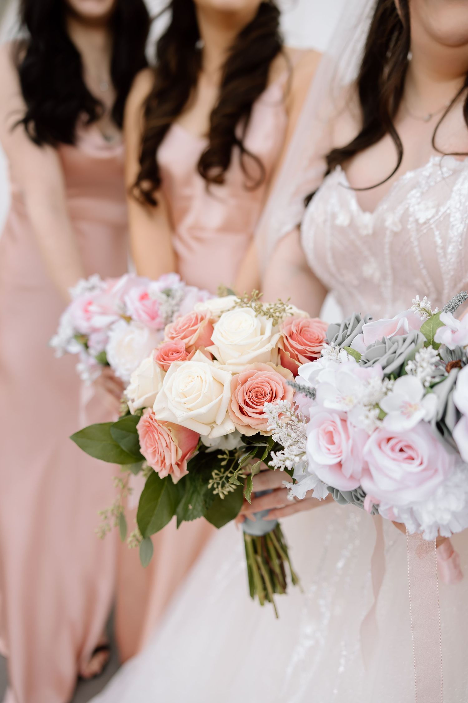 Bridesmaids in blush pink dresses hold elegant bouquets of pink and white roses with delicate greenery.