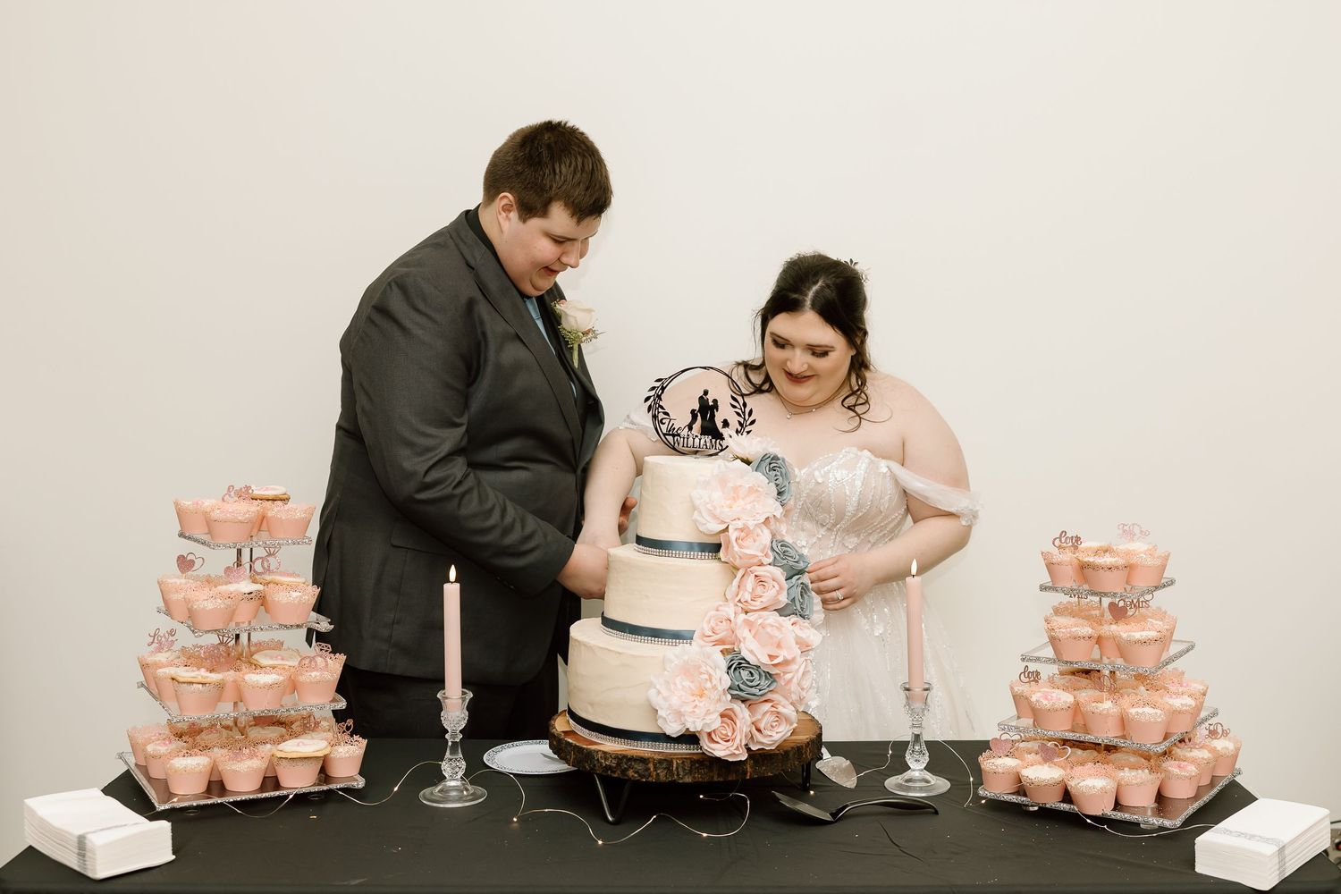 A couple cuts into their elegant three-tiered wedding cake adorned with pink and blue floral decorations.