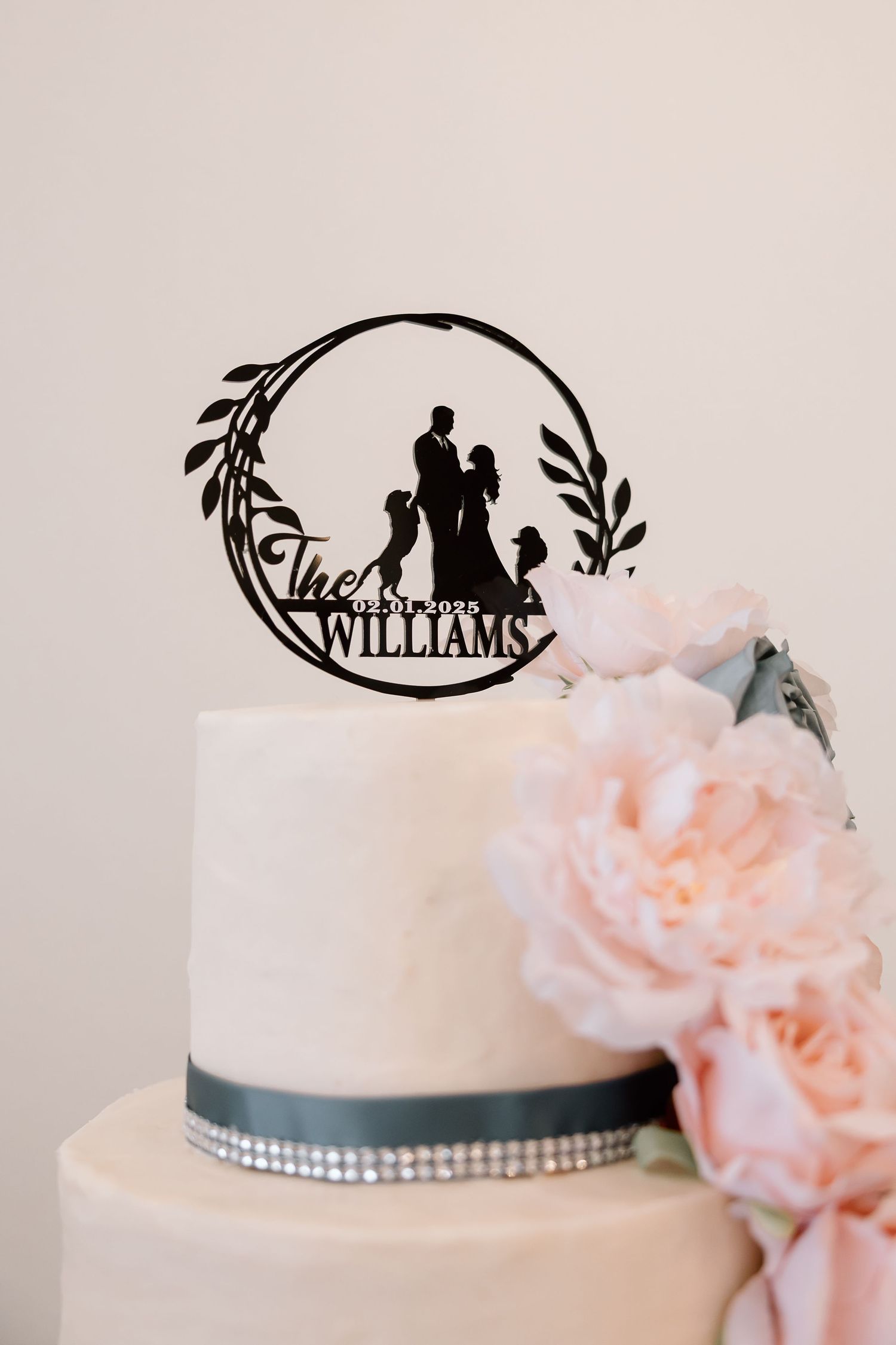 Elegant wedding cake details featuring pink flowers and a silver trim with a decorative black topper.