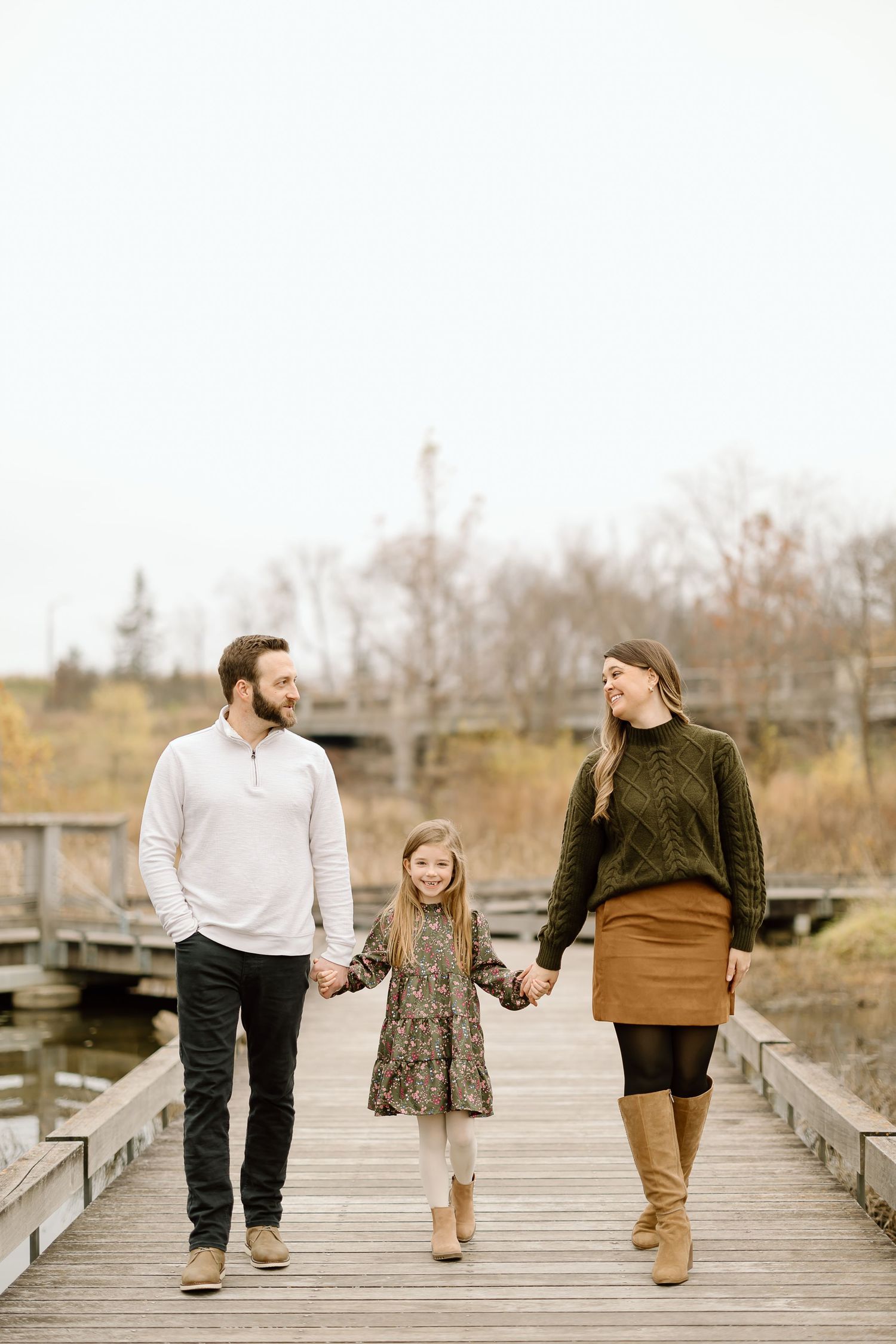 Family walking hand in hand on a wooden boardwalk during autumn wearing coordinated outfits.