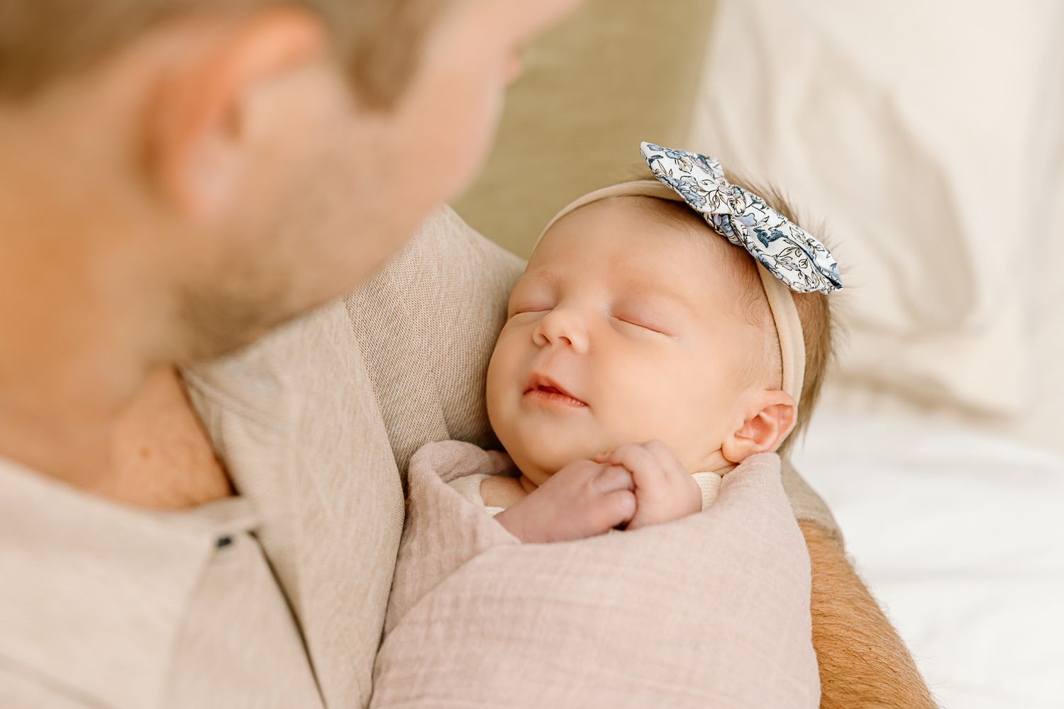 Sleeping newborn with sparkly bow headband resting on adult's shoulder.