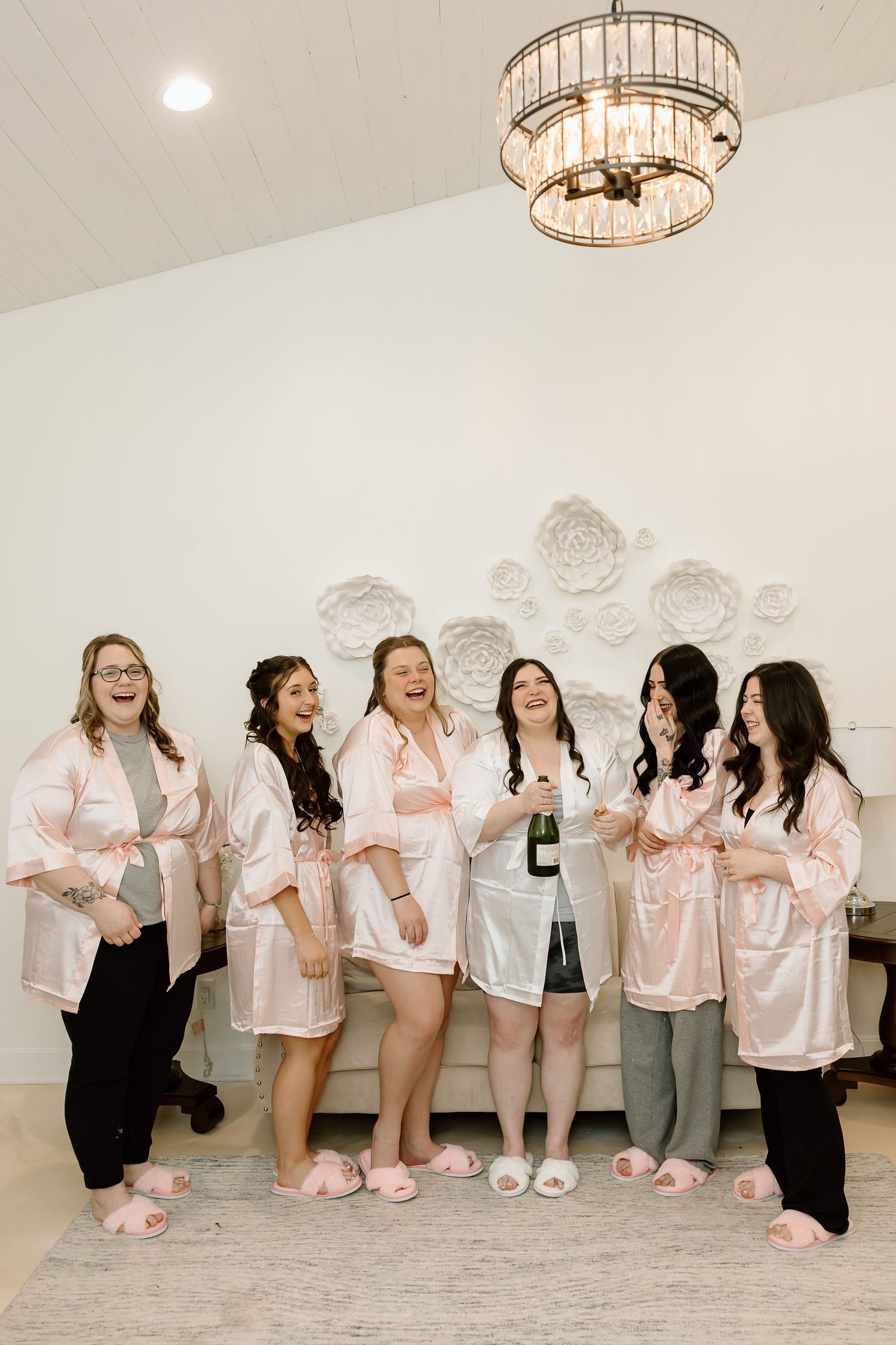 Bridal party in pink robes celebrates in getting ready room with champagne.
