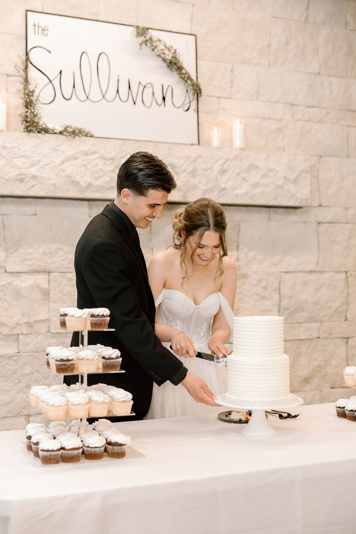 Newlyweds cut their white wedding cake together at reception with The Sullivan sign.