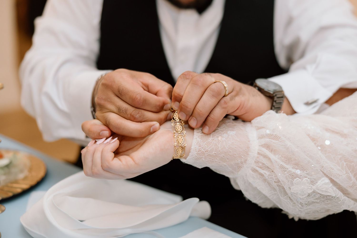 Groom fastening a gold bracelet on bride's wrist during wedding reception ceremony.