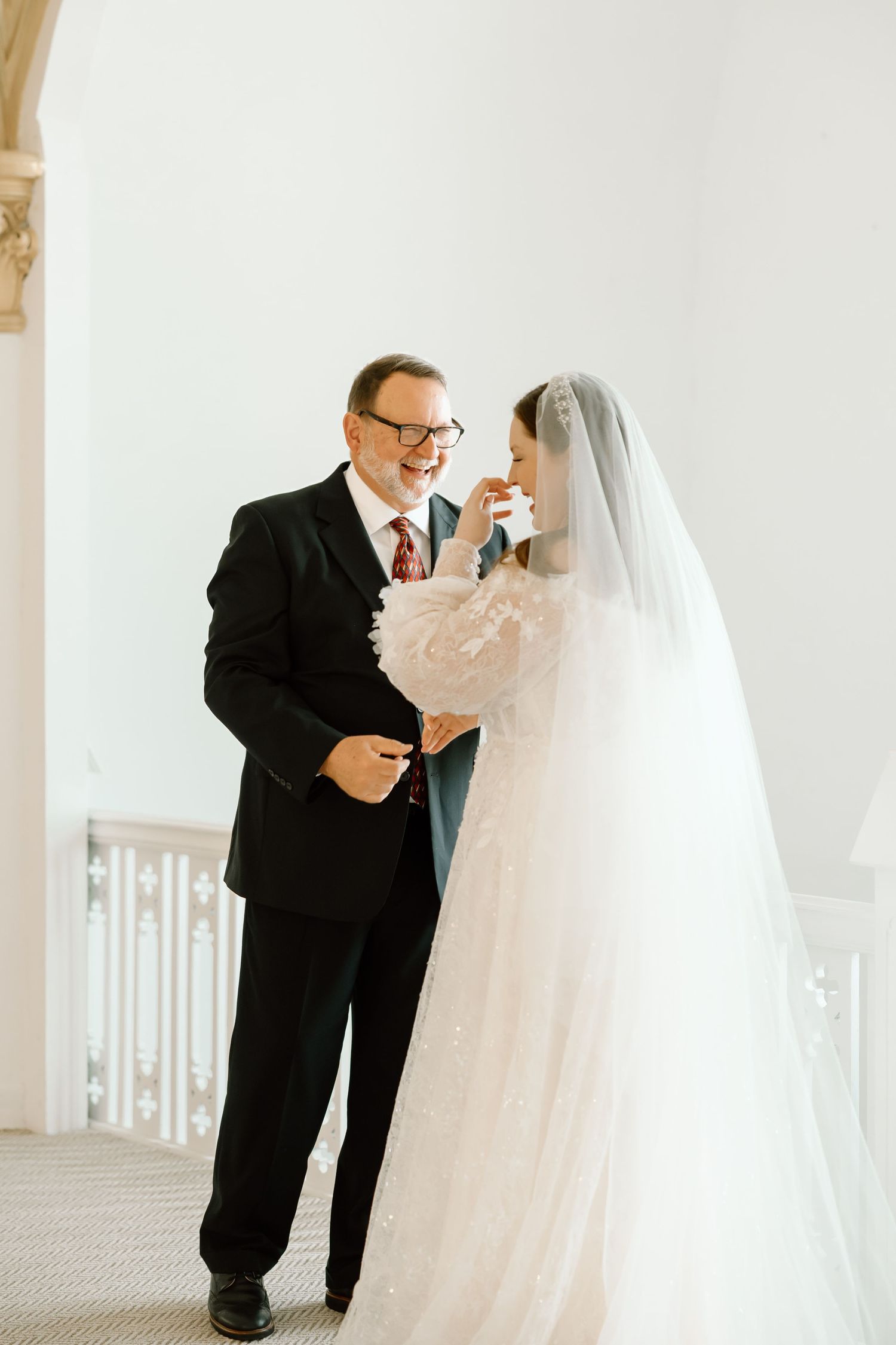 Father of the bride sharing an emotional first look moment with his daughter in a white lace wedding gown and veil.