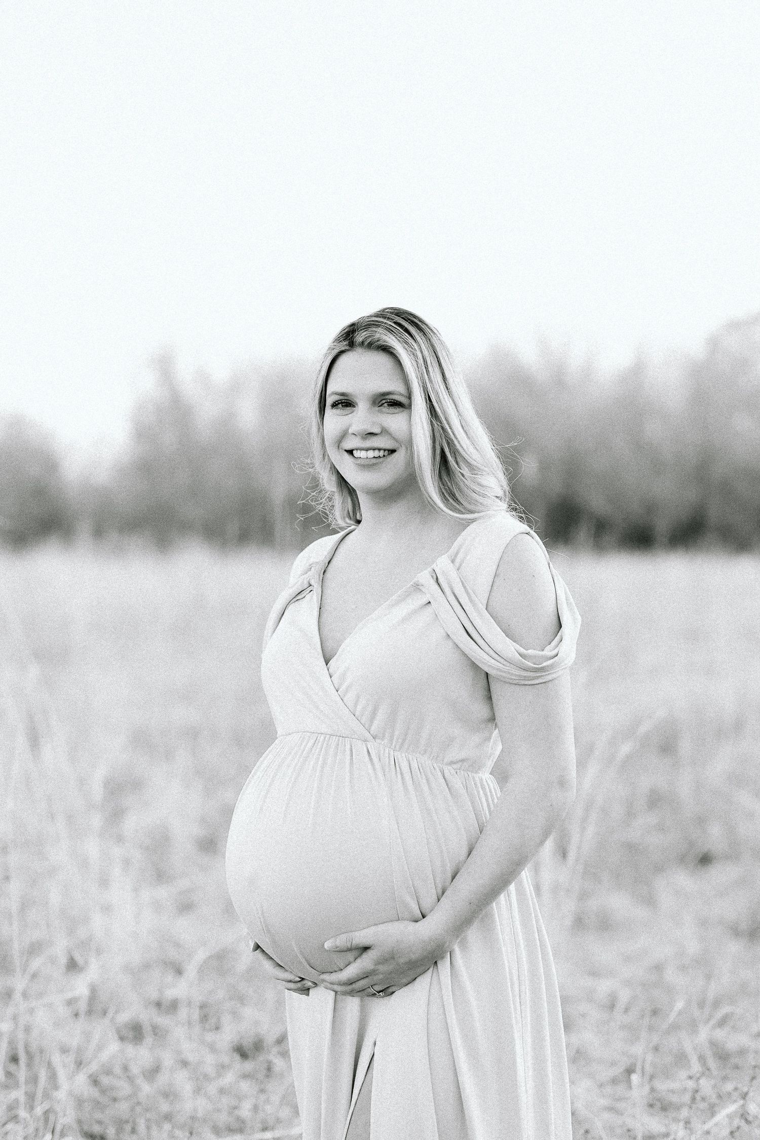A series of black and white maternity photos showing a woman in a flowing white dress standing in a misty field.