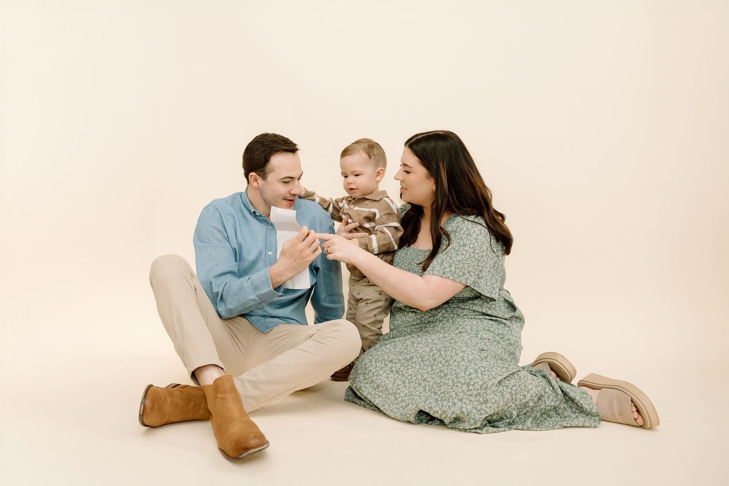 A family in coordinating outfits lounges together on a cream colored backdrop in a photography studio.