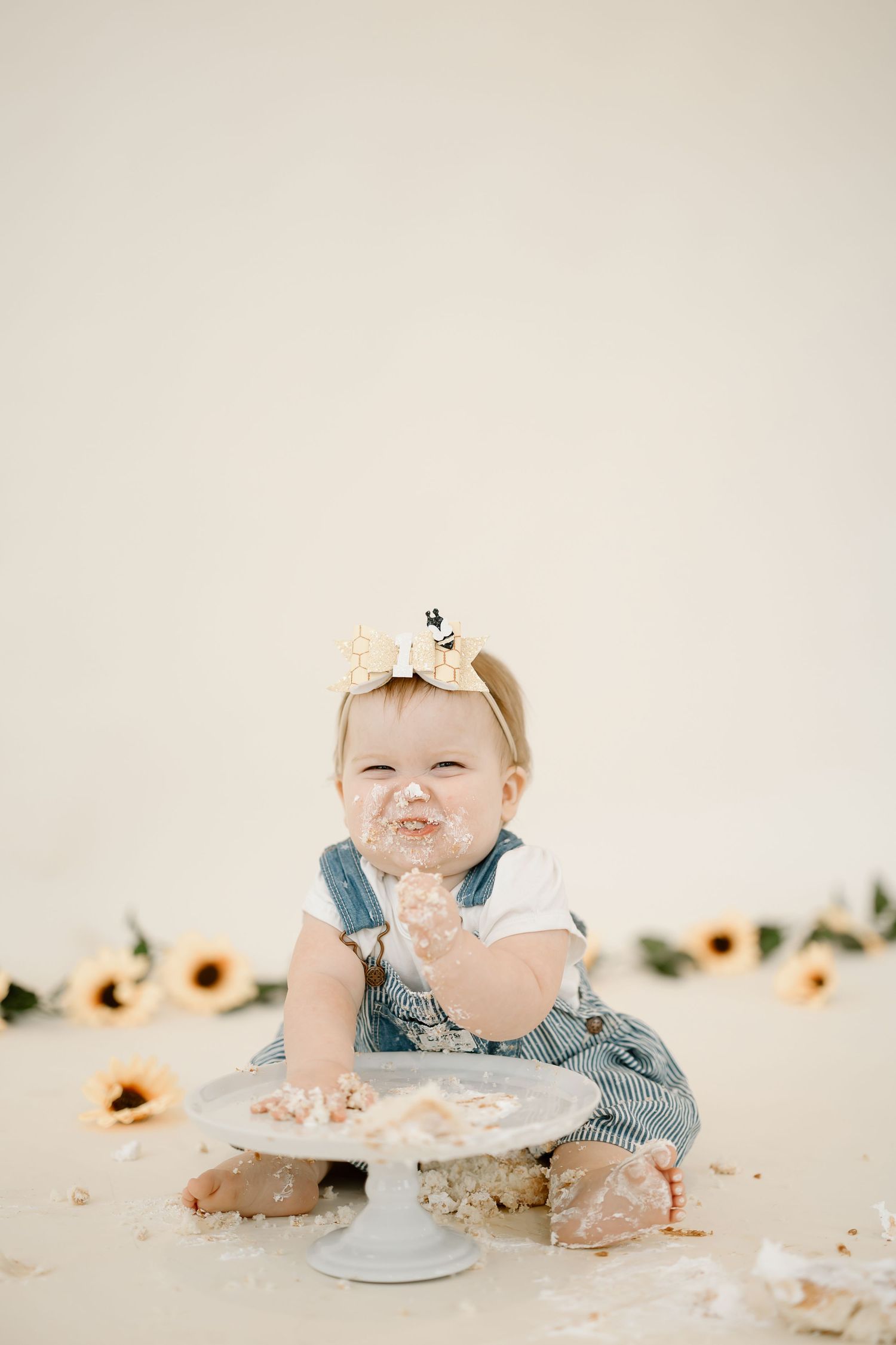 A series of four photos showing a baby in blue clothing having a messy cake smash photo session with a white cake.