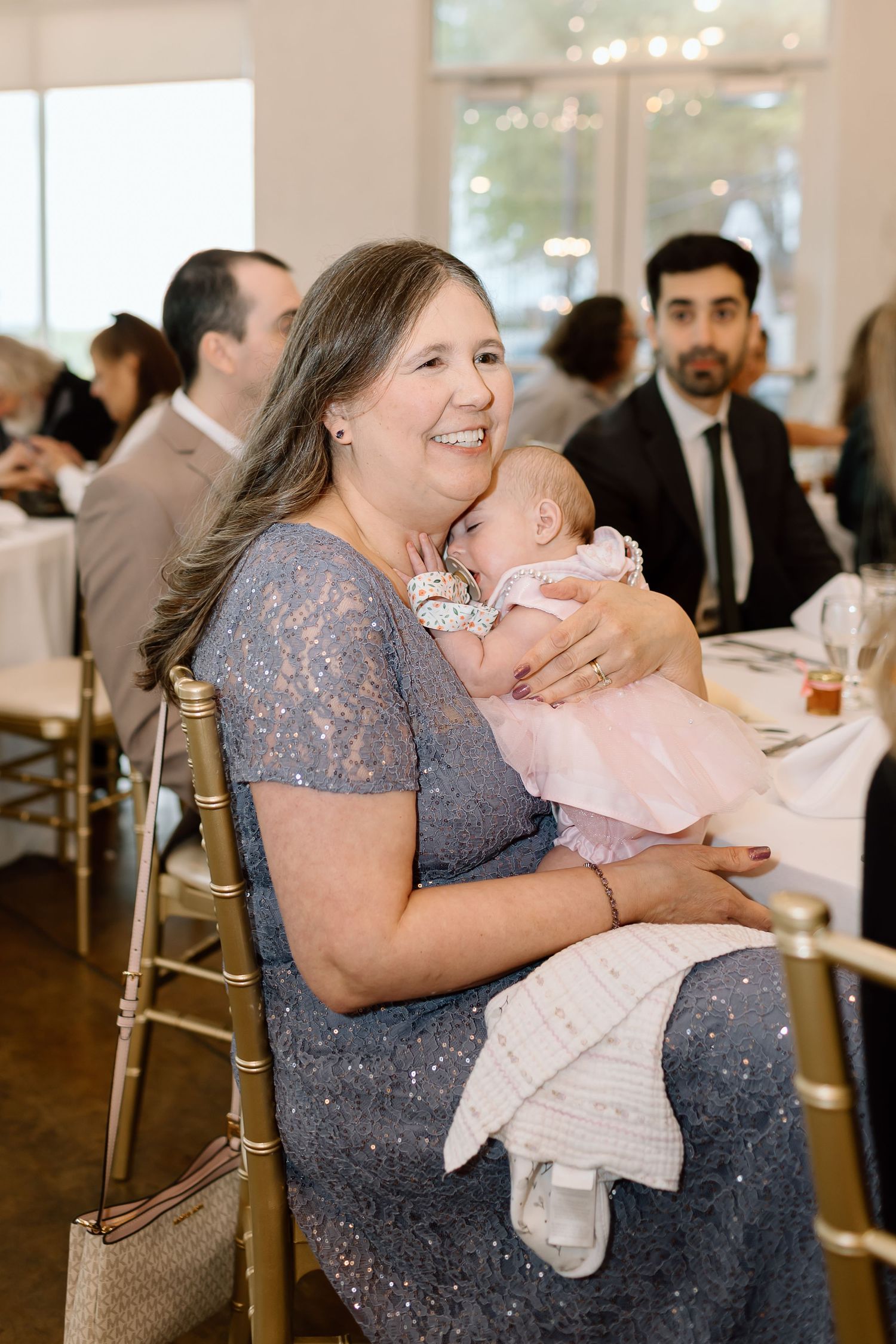 A series of candid reception moments showing a guest in a blue dress holding and embracing a baby in pink.
