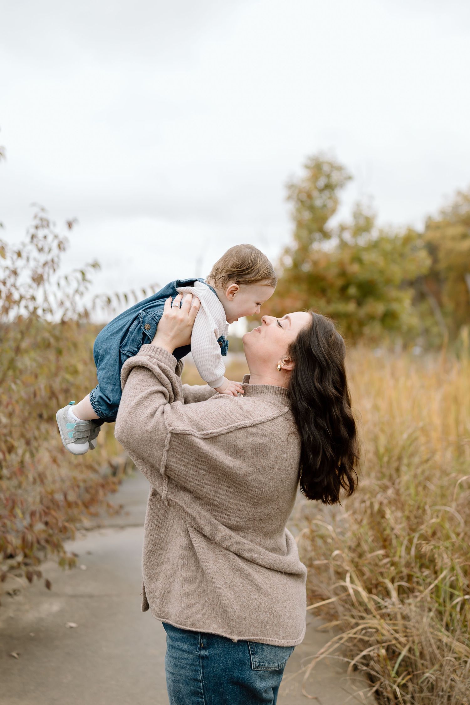 Parent and child playing together in a field of tall grass on an autumn day.