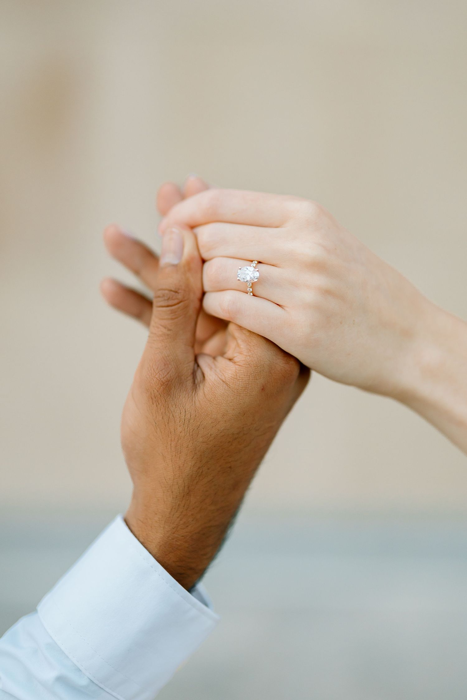 Close-up sequence of hands exchanging a diamond engagement ring against a soft beige background.