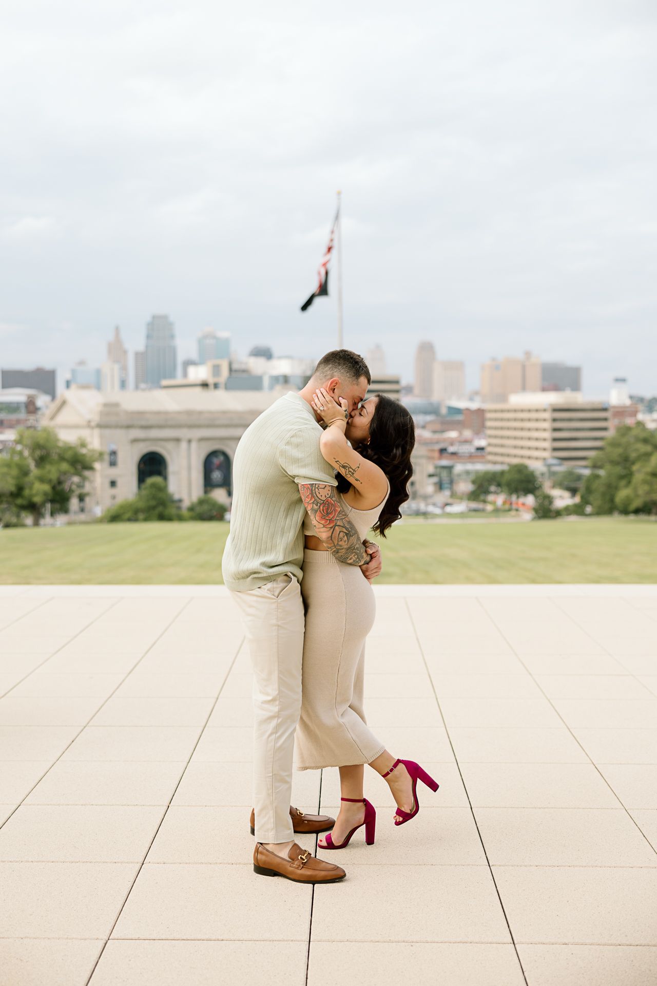 A romantic couple embraces on an outdoor terrace with the Kansas City skyline visible in the background.