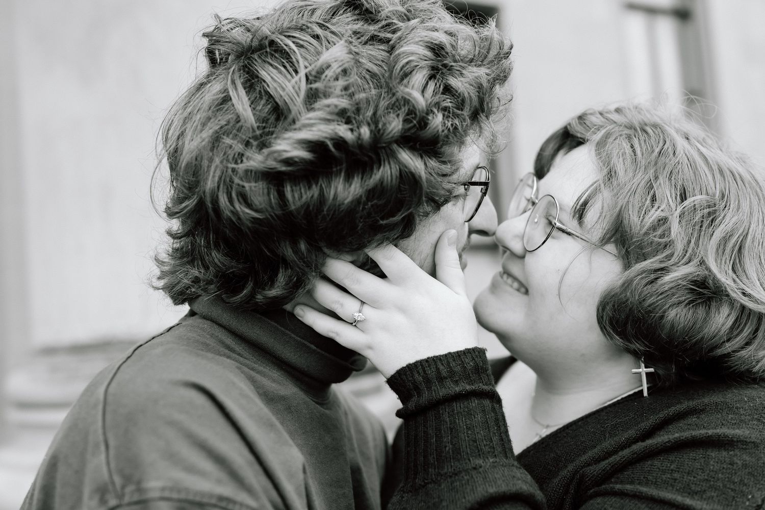 A tender black and white photograph shows an intimate moment between two people wearing glasses.