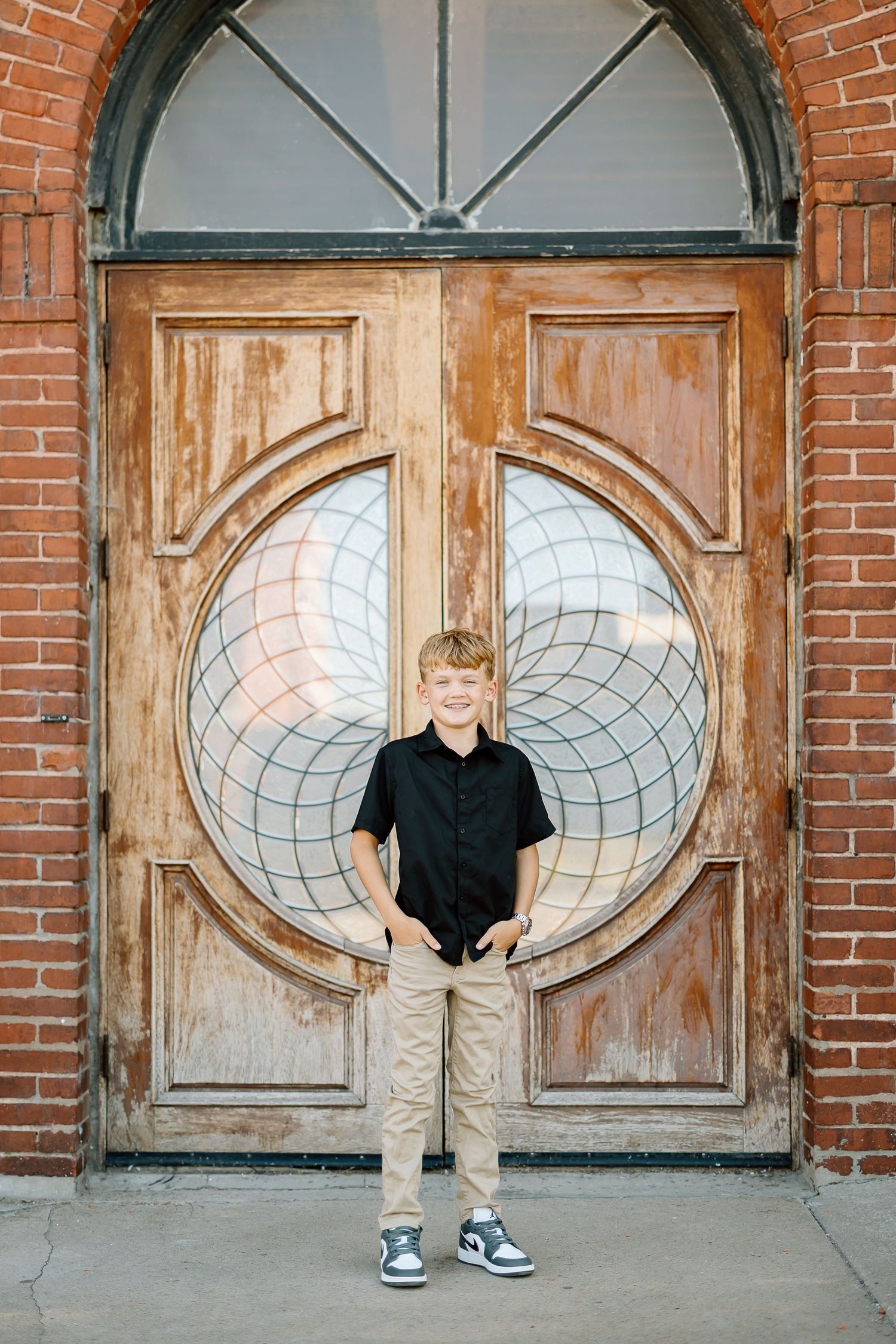 A panoramic photo showing three vintage wooden doors with oval glass windows set in a red brick wall.