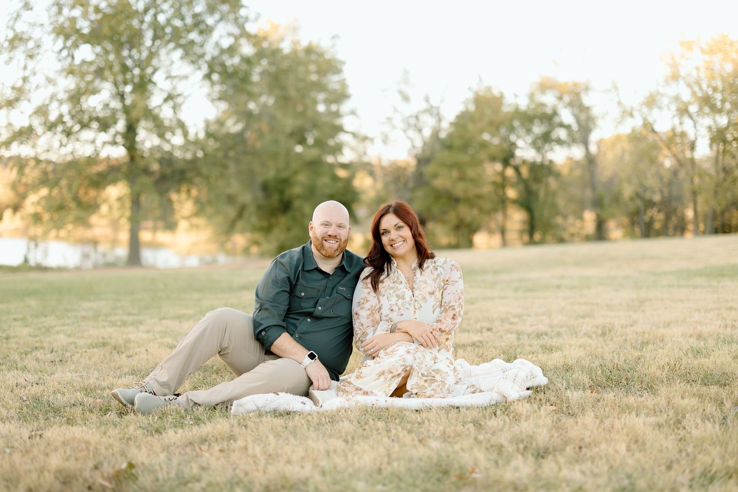 Romantic couple lying together in a sunlit grassy field during golden hour photography session.
