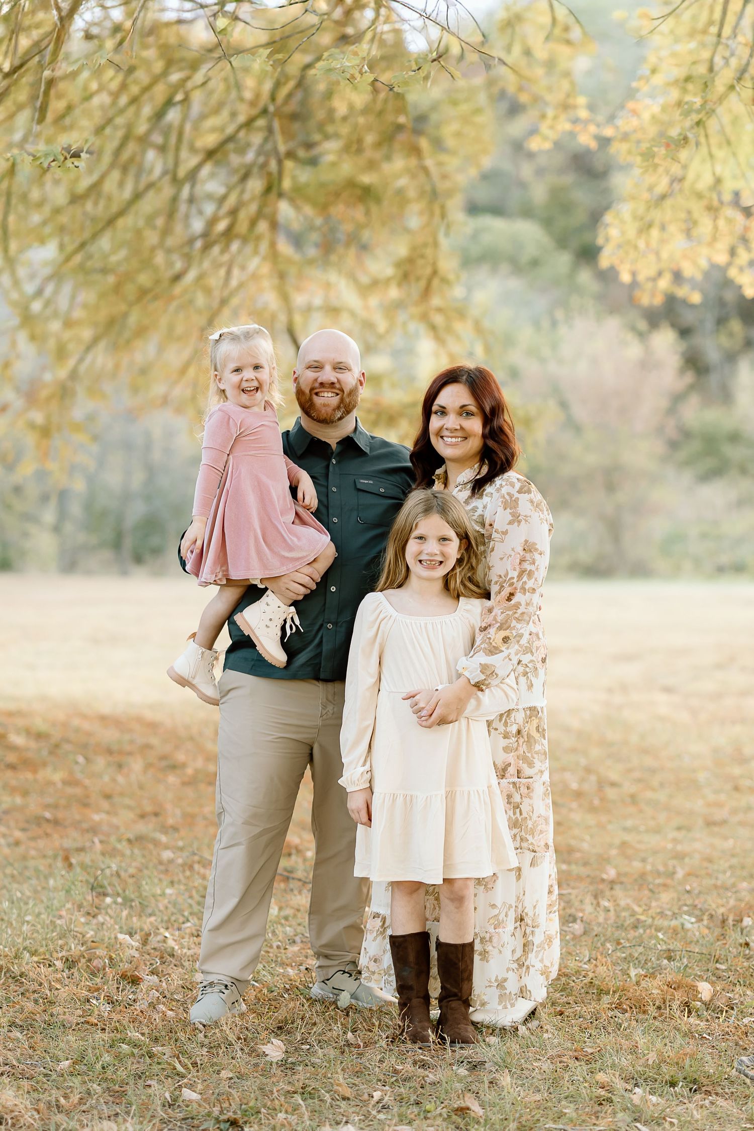 A family poses together outdoors in coordinated neutral outfits against a backdrop of golden autumn foliage.