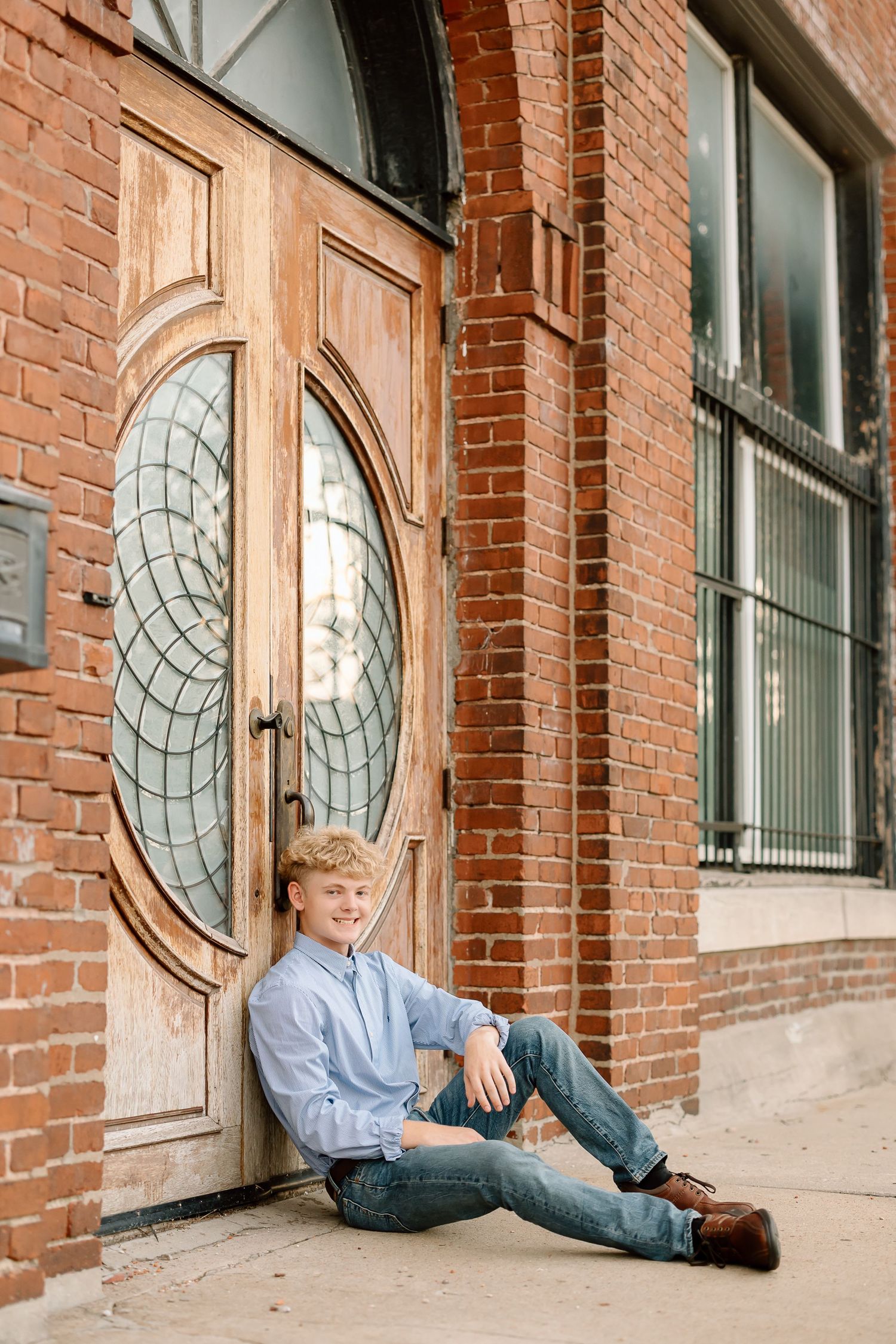 Person in blue shirt and jeans sits against brick wall with circular window panels in progressive sequence.