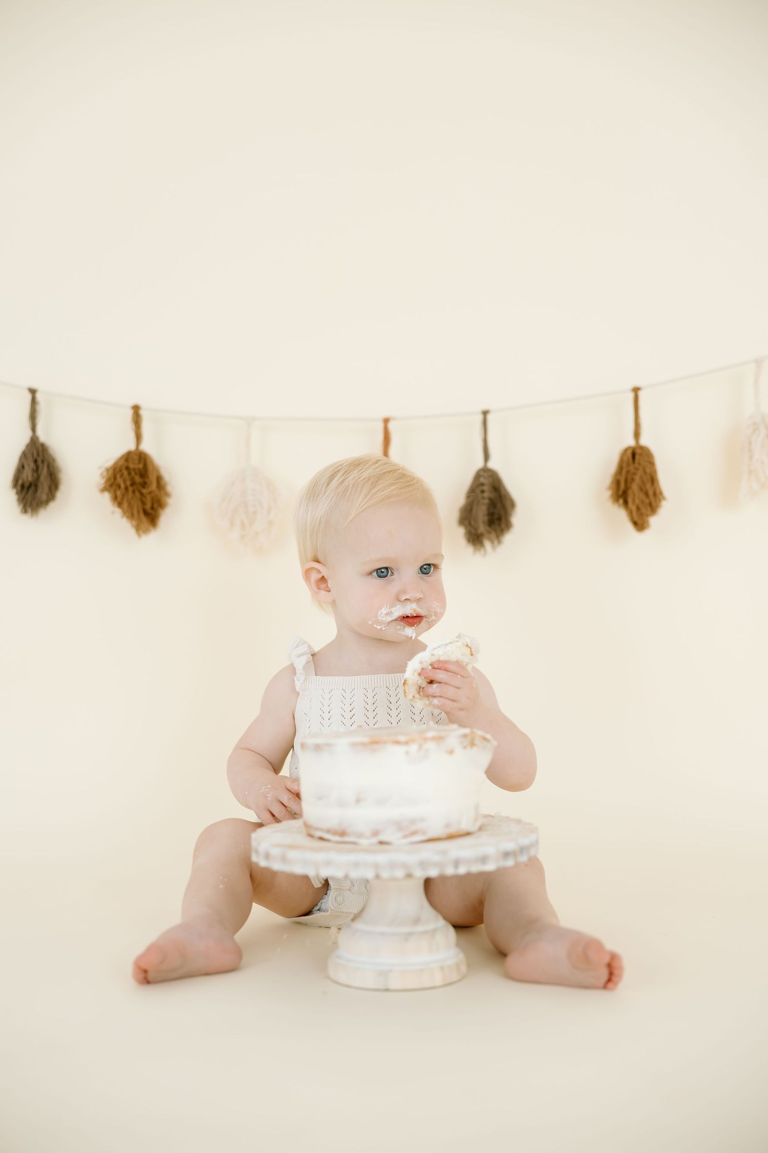 A series of photos showing a baby in white celebrating with a cake while feathers hang decoratively on a string above.