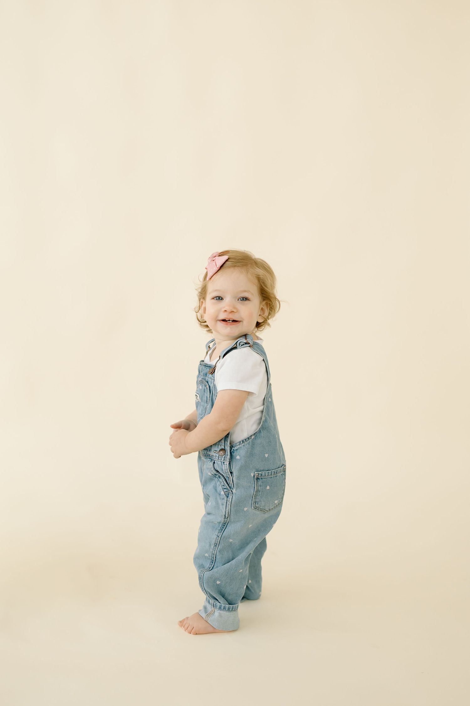 A series of playful poses showing a toddler in denim overalls against a light beige backdrop.