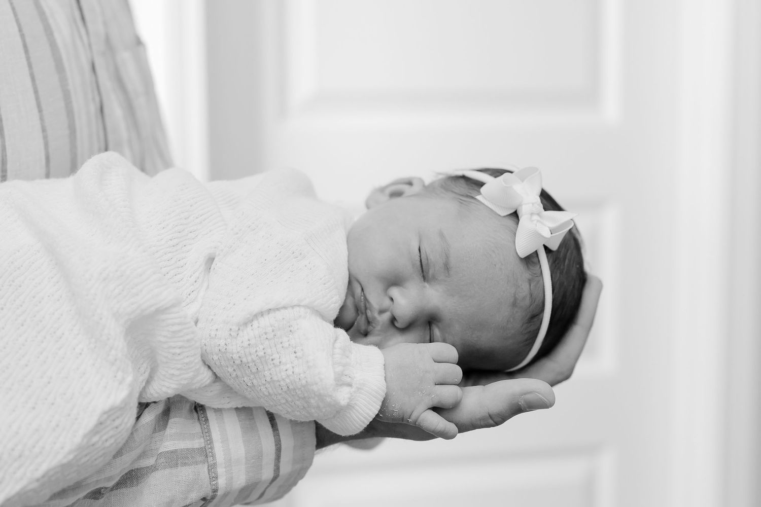A series of black and white newborn photos showing a sleeping baby wrapped in soft white blankets.