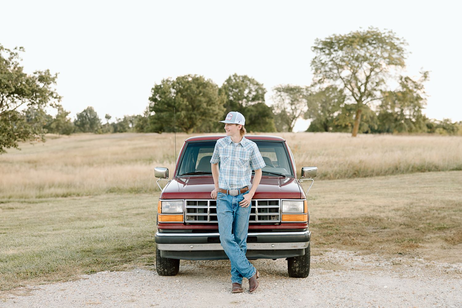 Classic pickup truck parked in a grassy meadow with scattered trees on a sunny day.