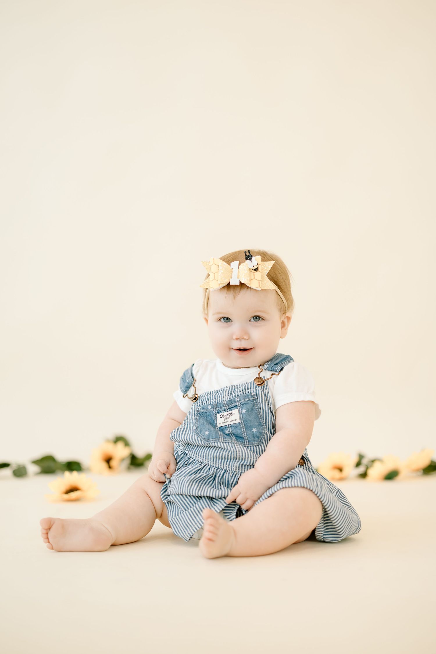 A series of four studio portraits showing a baby in blue overalls sitting against a cream backdrop with peach flowers.
