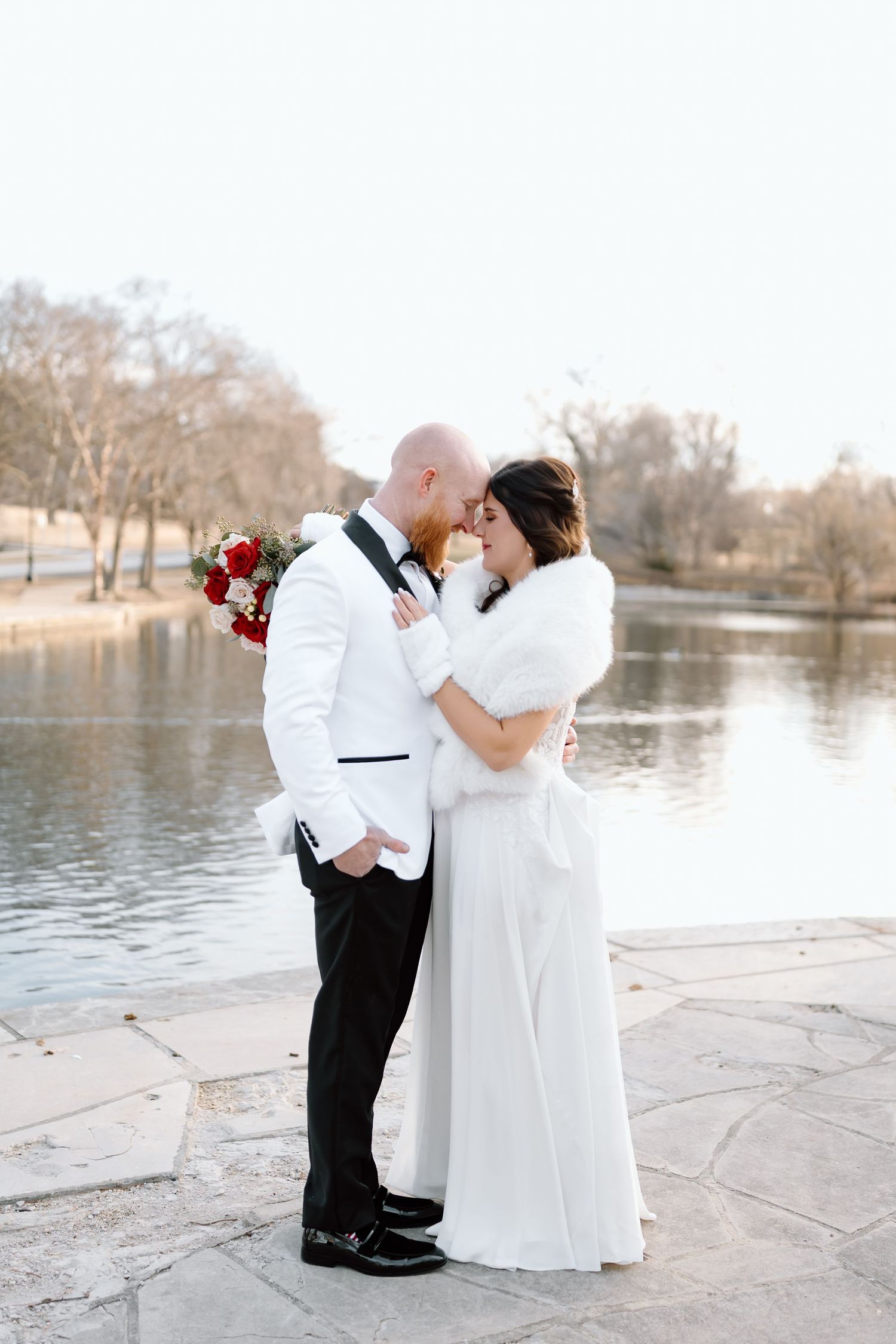 A couple in wedding attire shares a romantic moment by a serene lake on their special day.