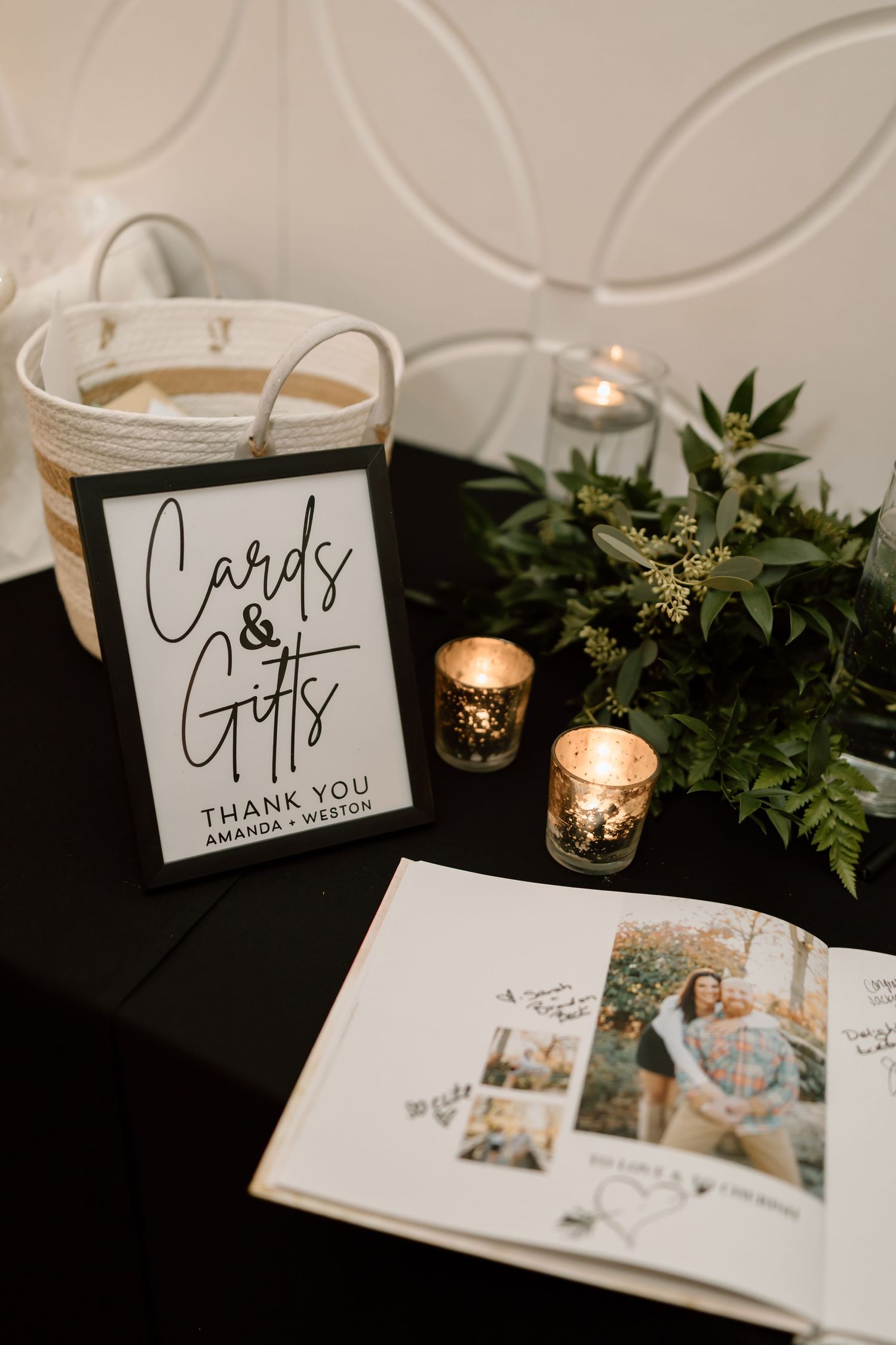 Wedding reception table details with cards, candles, and greenery decorations arranged elegantly on a black tablecloth.