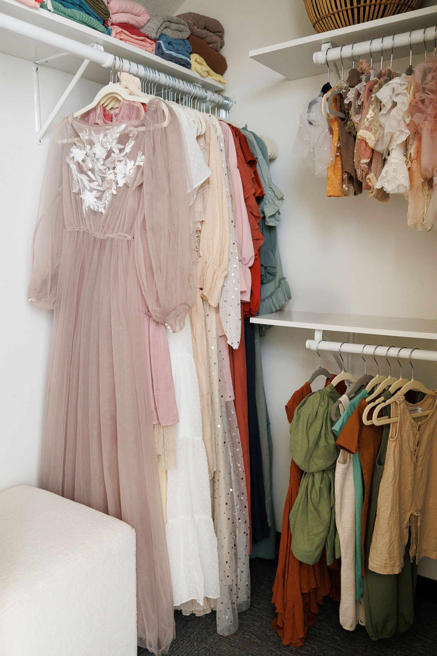 Organized walk-in closet featuring feminine dresses in soft pastels, whites, and earth tones hanging neatly on white rods.