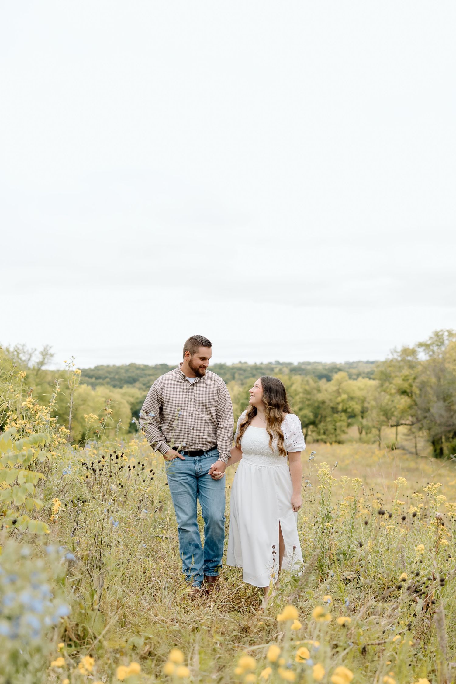 Couple walking through a field of yellow wildflowers on a sunny autumn day.