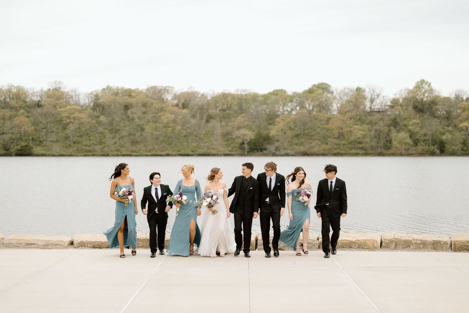 Wedding party stands in a line against a scenic lake backdrop.
