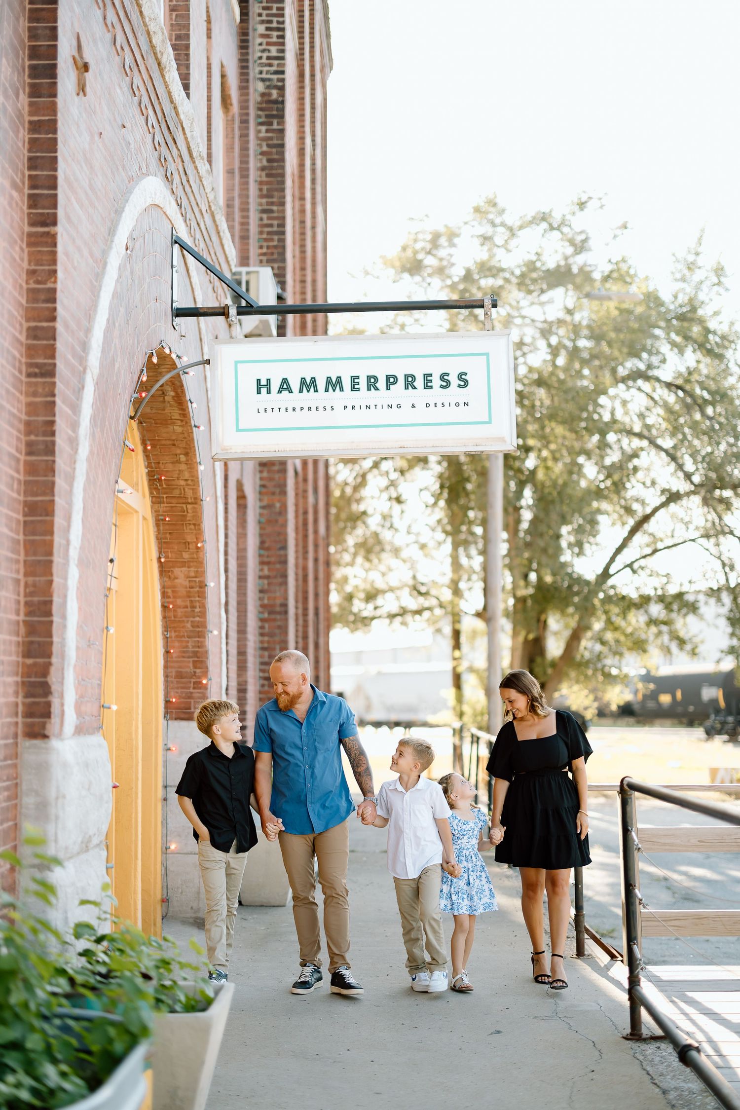 Family walking together under covered brick walkway of historic Hammerpress building during outdoor photo session.