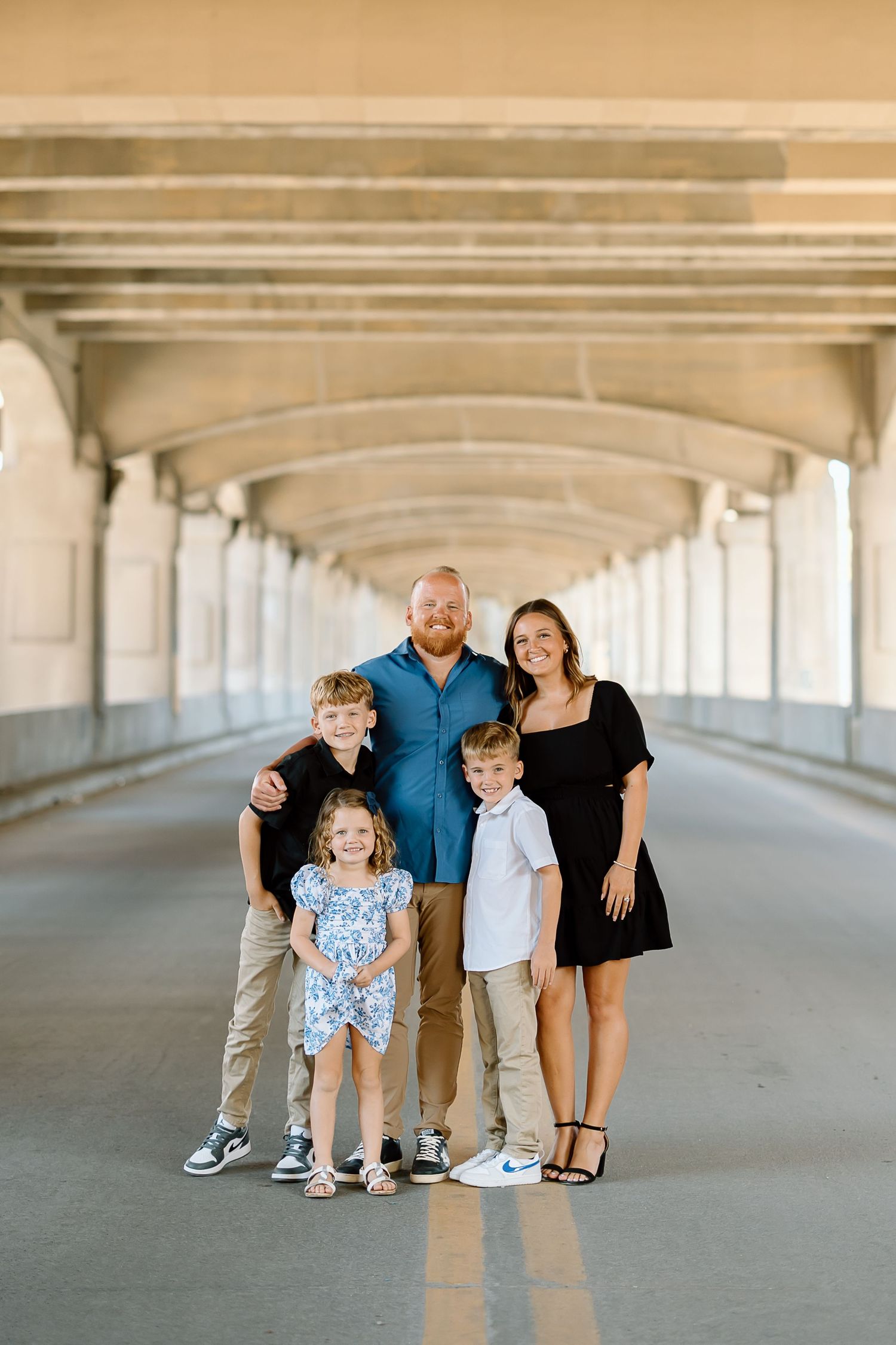 Family poses together in a covered outdoor walkway with white arched columns and concrete floors.