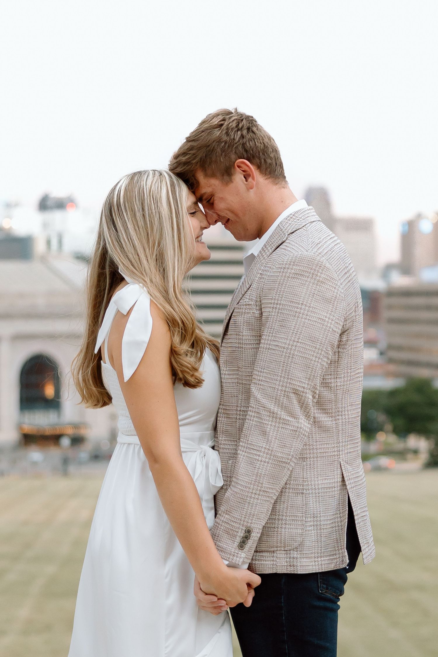 A romantic couple shares an intimate moment outdoors with a cityscape backdrop.