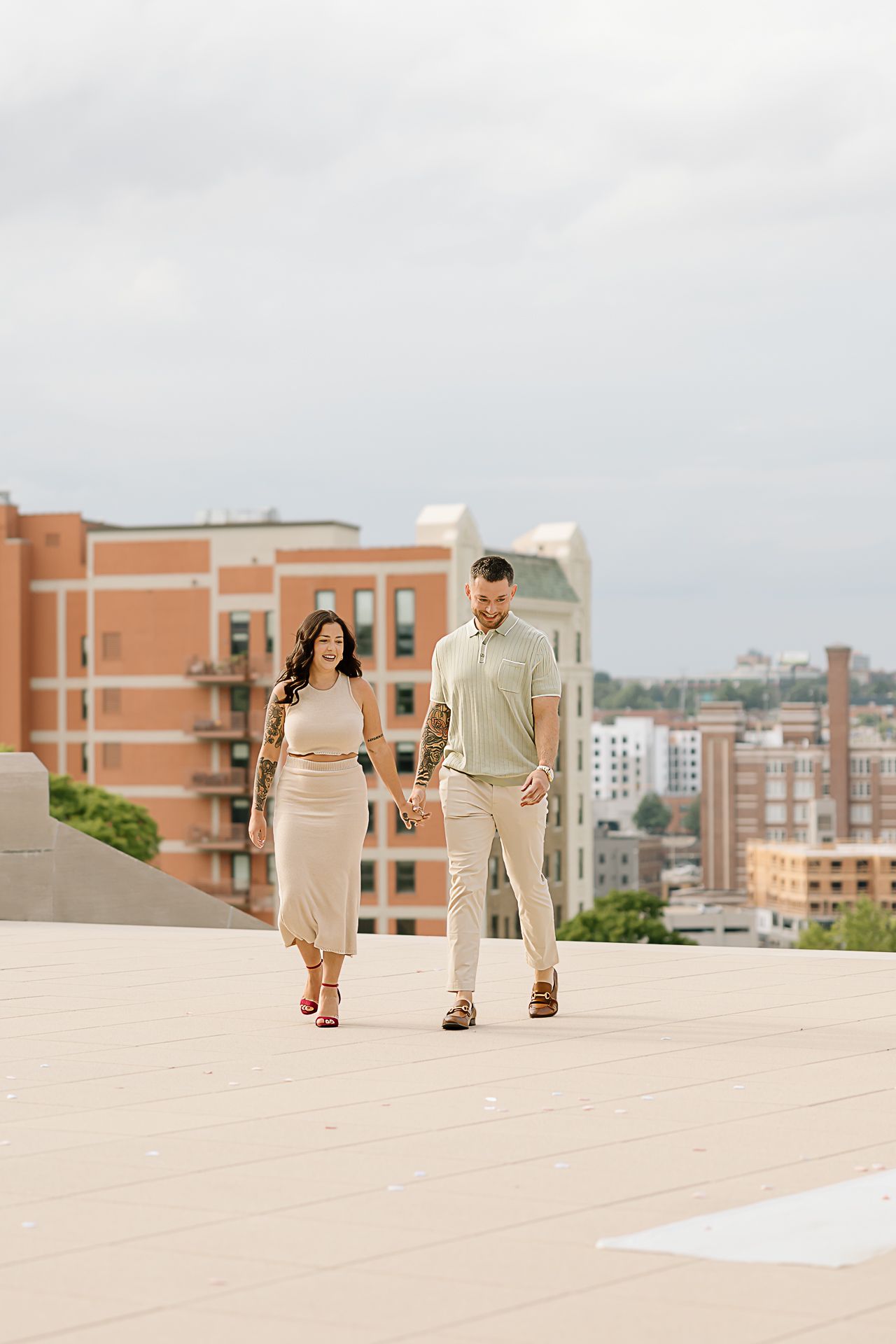 Couple walking together on a bright rooftop terrace with brick buildings in the background.