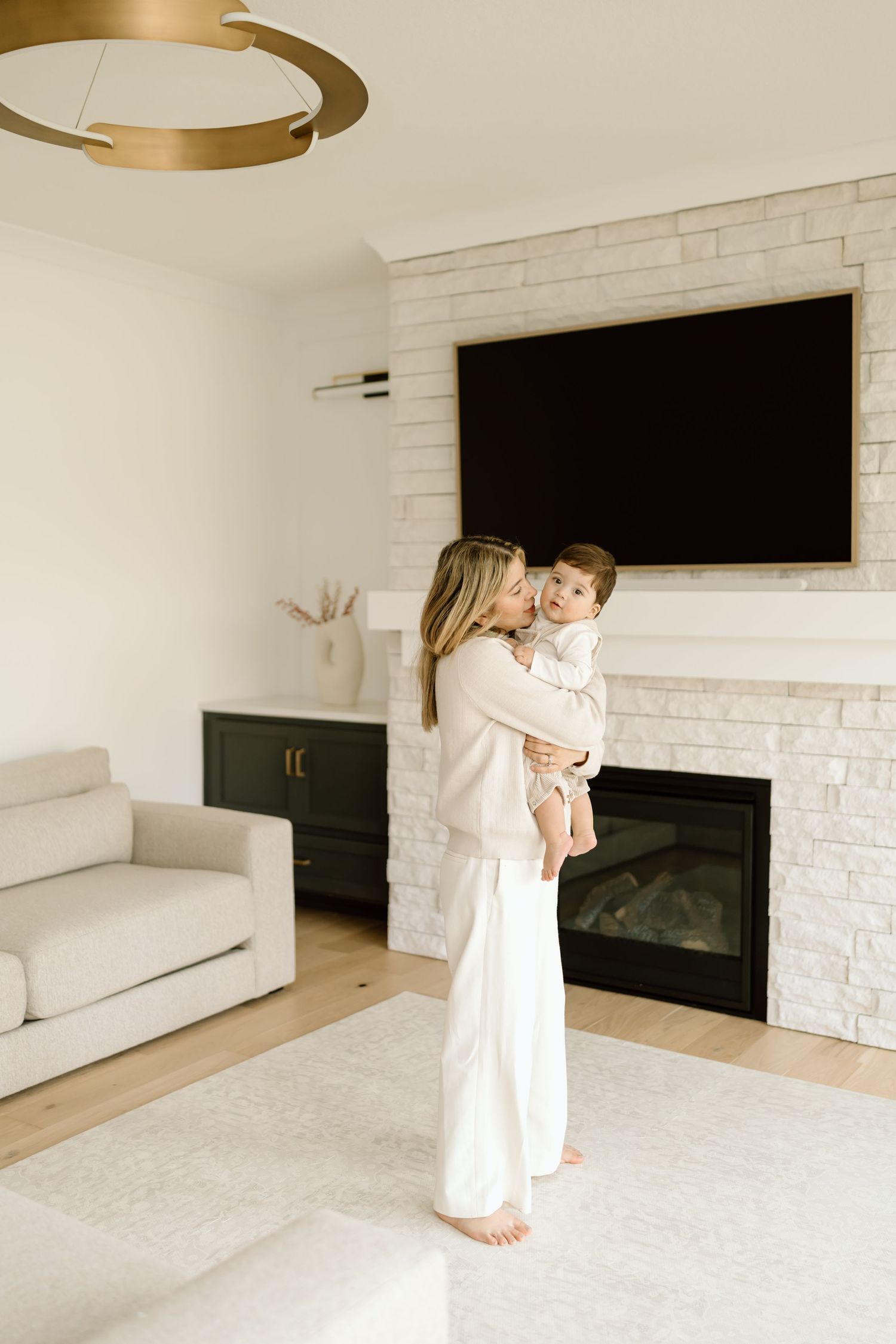 A cozy living room interior with white brick fireplace, mounted TV, modern lighting and plush carpet.