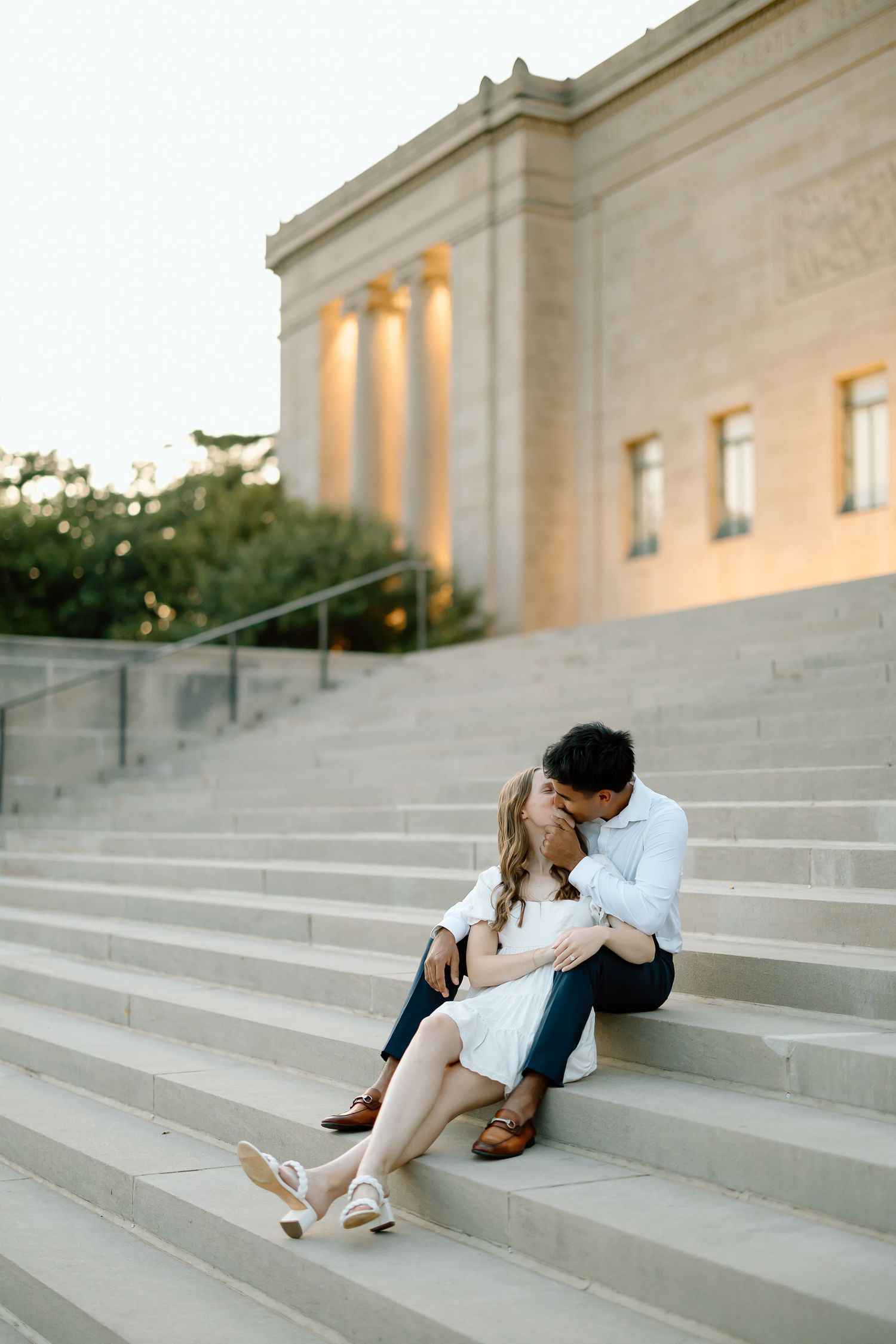 A couple shares a romantic moment while sitting on grand stone steps of a classical building at dusk.