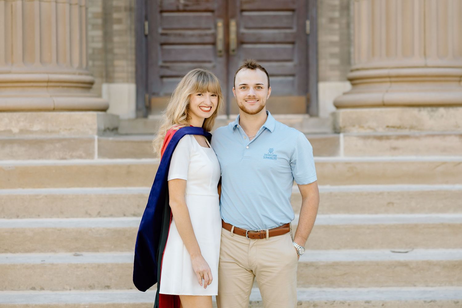 Students in casual attire stand in front of ornate stone columns at a university campus entrance.