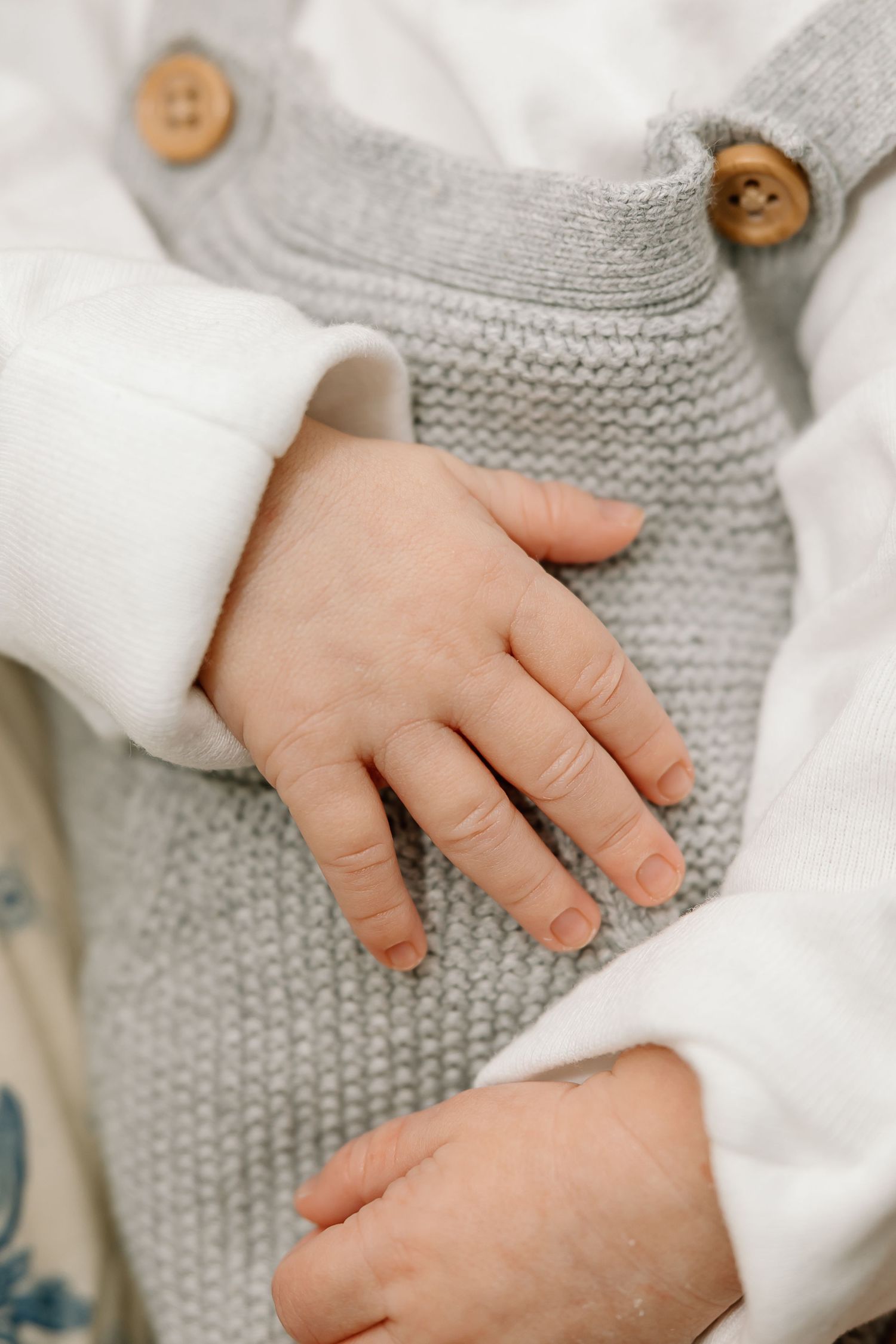 Small baby hand resting on gray knitted fabric with wooden buttons and white clothing.